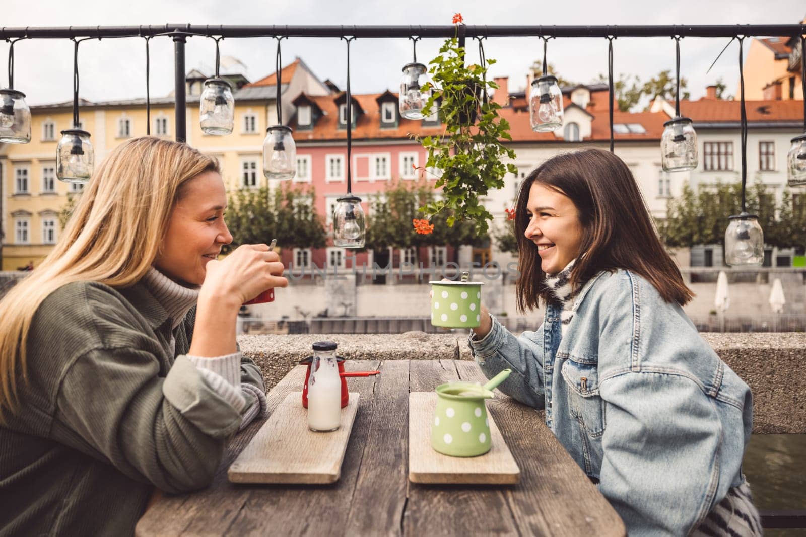 Couple of best friends meeting for a coffee date sitting outside at a cafe in the city center by VisualProductions