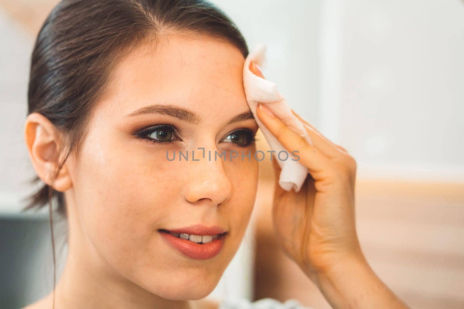 Close up woman removing make up off her face using micellar water on a cotton pad by VisualProductions