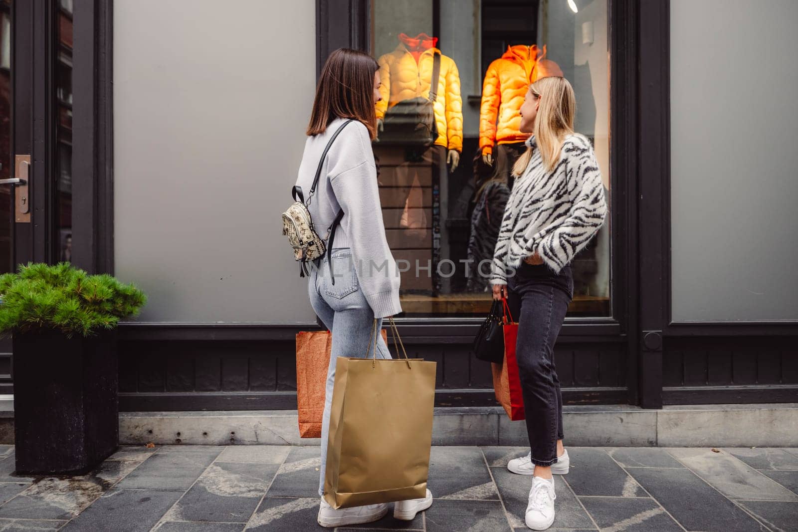 Two best friends having a fun day shopping in the city center, looking at the window display of clothing store by VisualProductions
