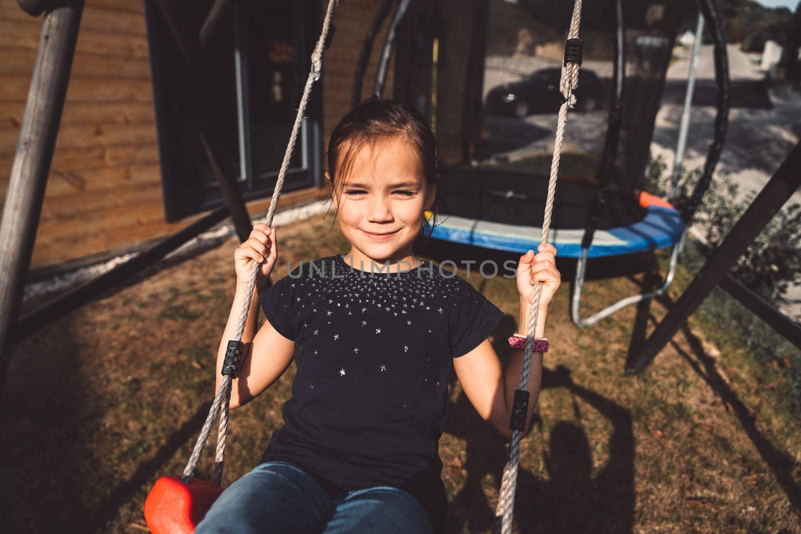 Smiling young girl enjoying time outside, playing on a swing on a sunny summer day by VisualProductions