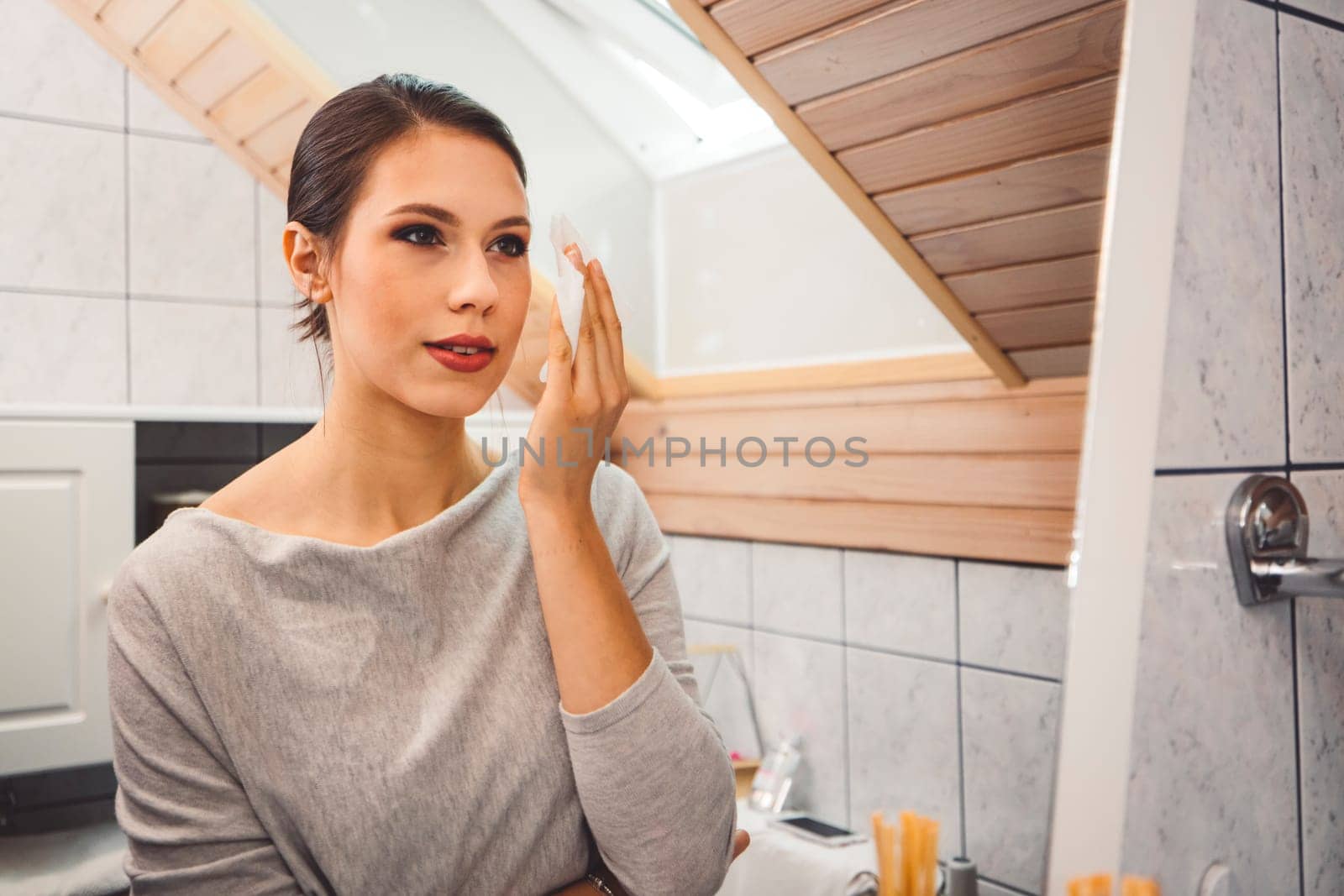 Beautiful young woman cleaning make up off her face using a cotton pad by VisualProductions
