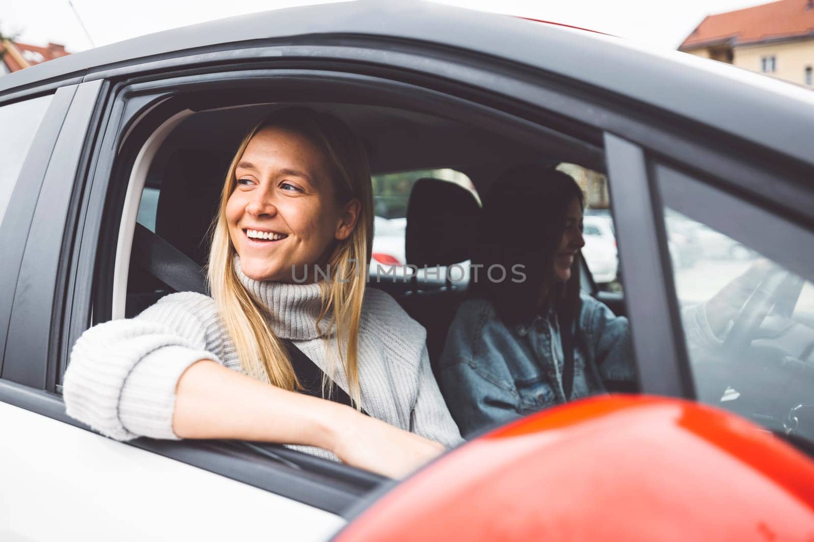 Blonde woman with a big smile on her face sitting in the car looking out the window while parked in the parking lot by VisualProductions