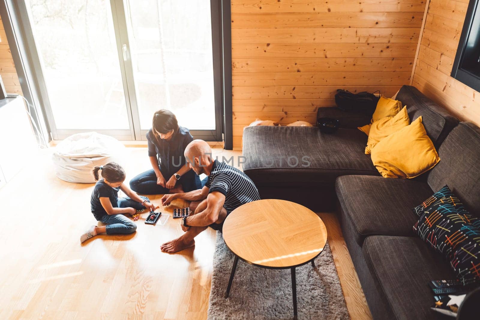 Family of three with young girl playing games on the floor in the living room, spending time together over the weekend by VisualProductions