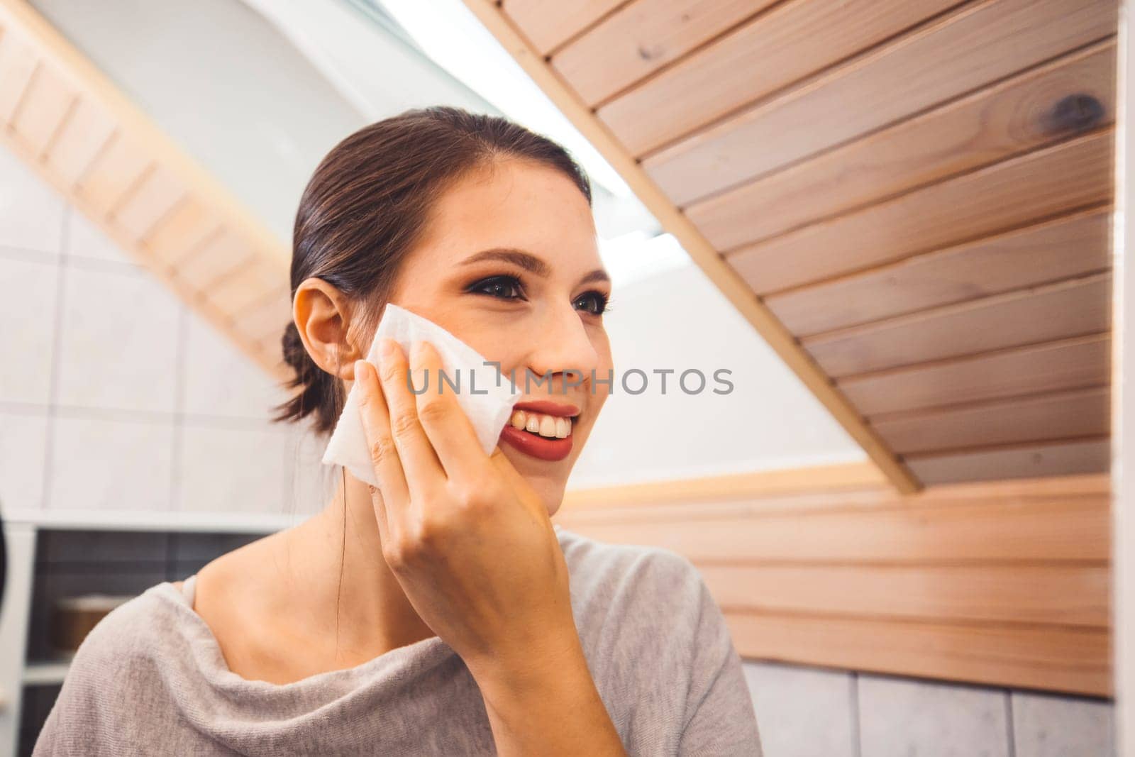 Waist up portrait of a woman standing in front of a mirror cleaning make up off her face by VisualProductions