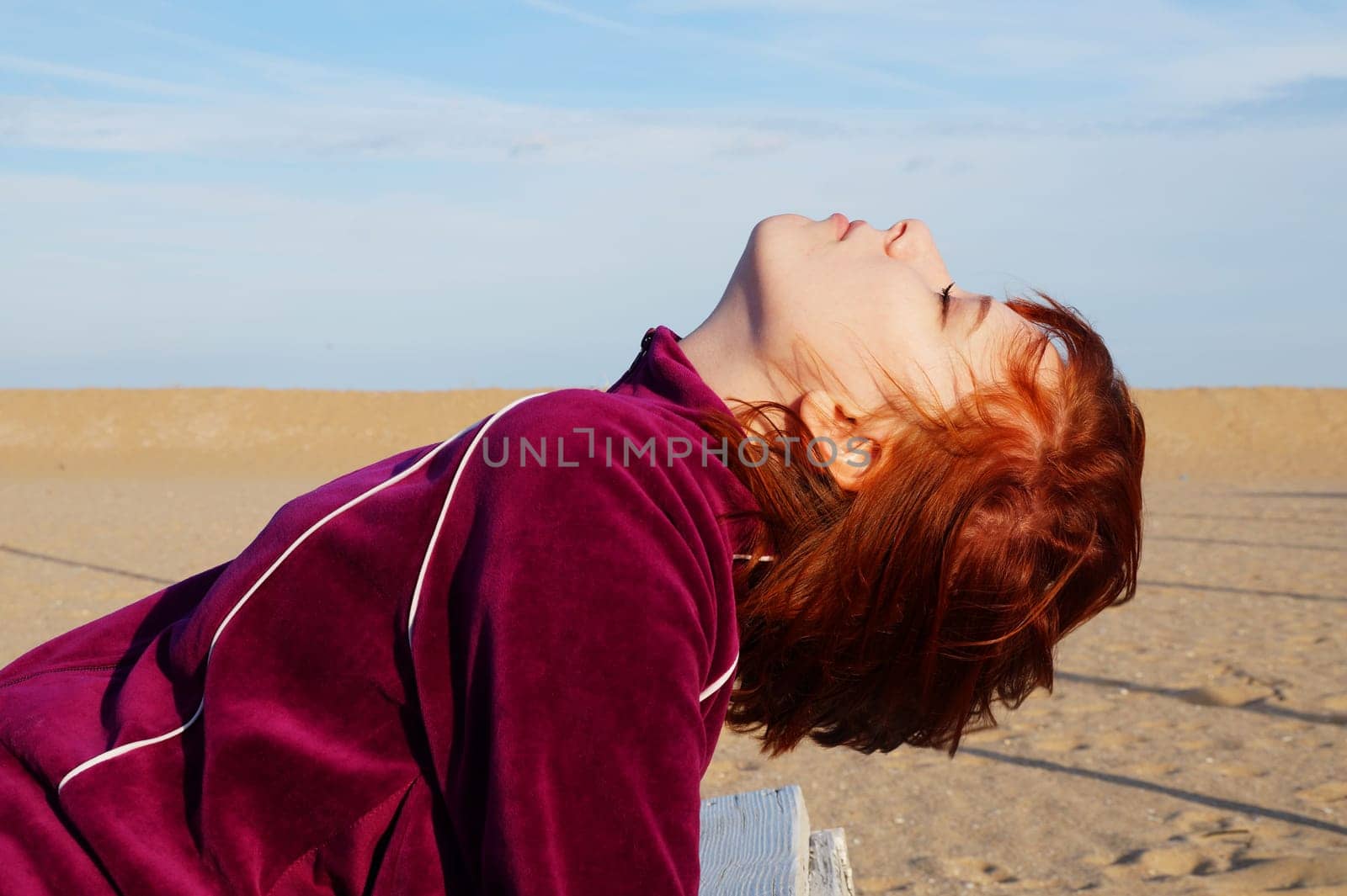 Portrait of a red-haired teenage girl with closed eyes and head thrown back on an empty beach by Annado