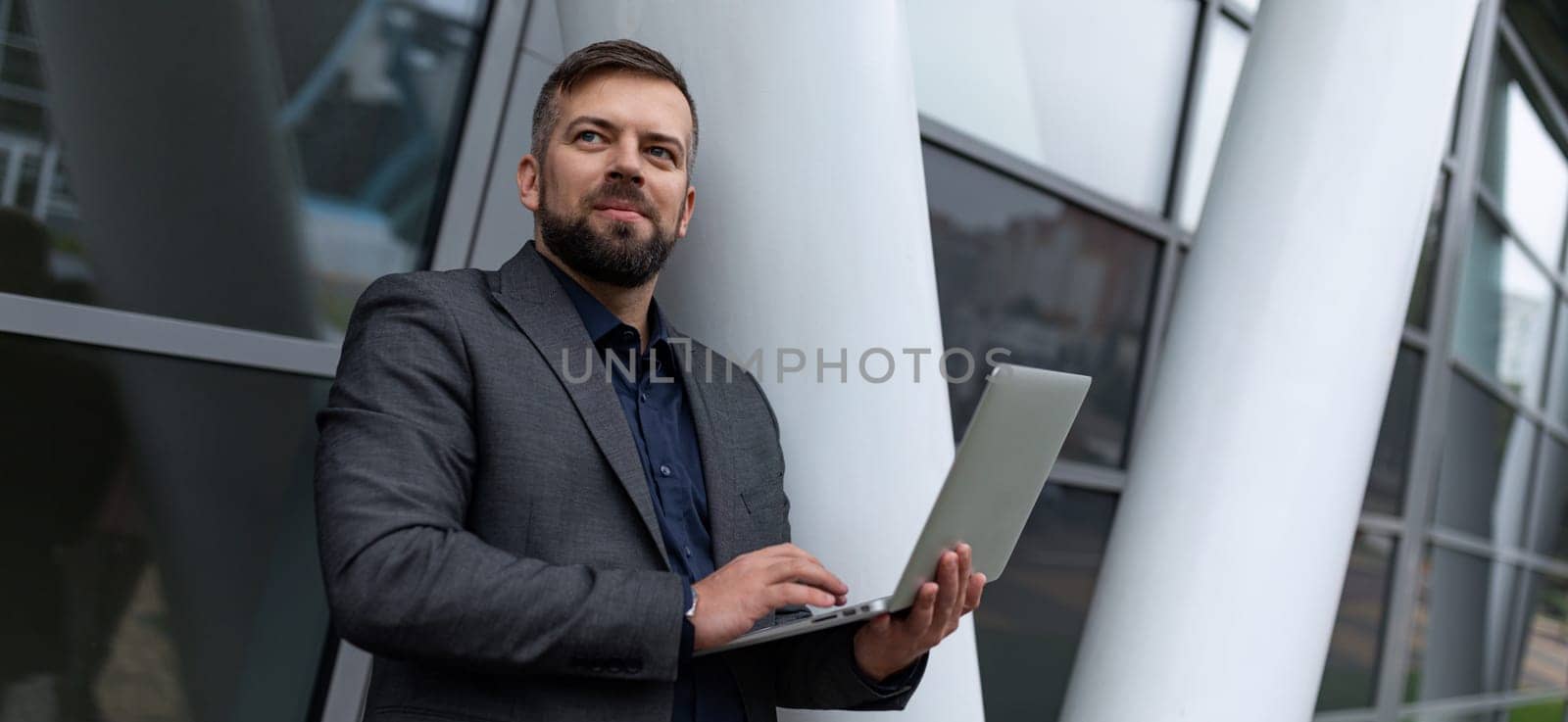 pensive male architect with a laptop works on the background of the building.