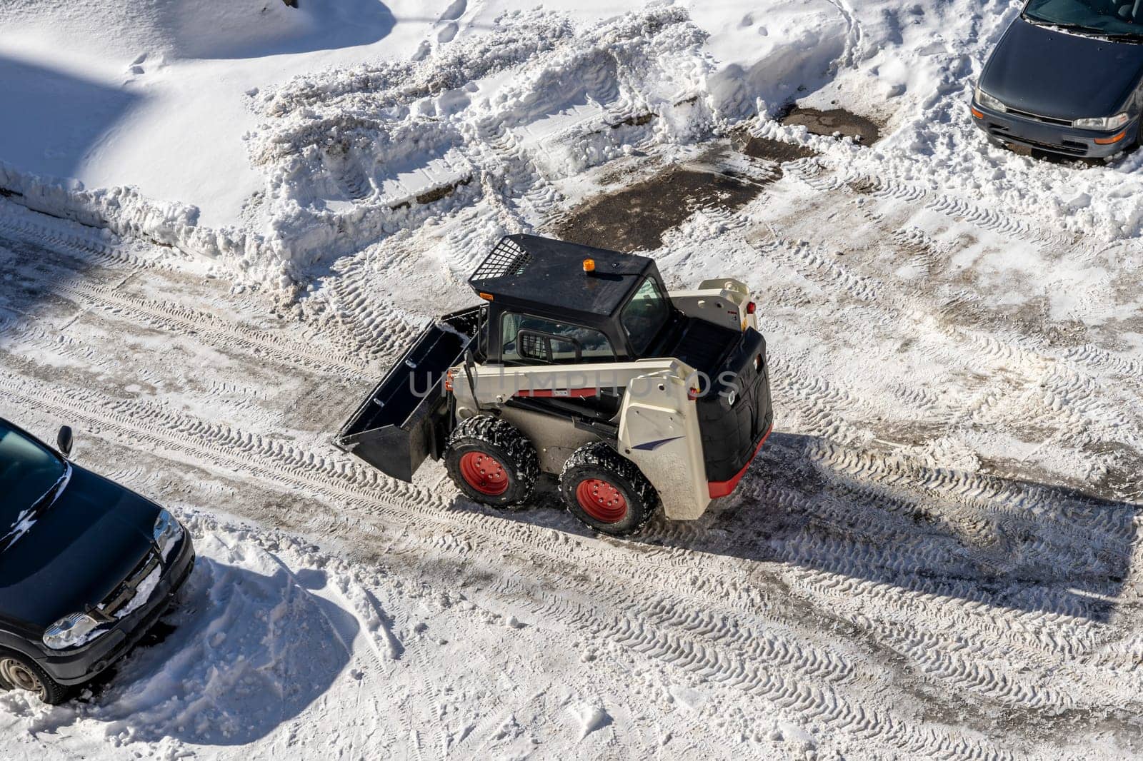 a small snowplow with a bucket cleans yard roads from snow. Maintenance of the territory. city snow cleaning service department at work