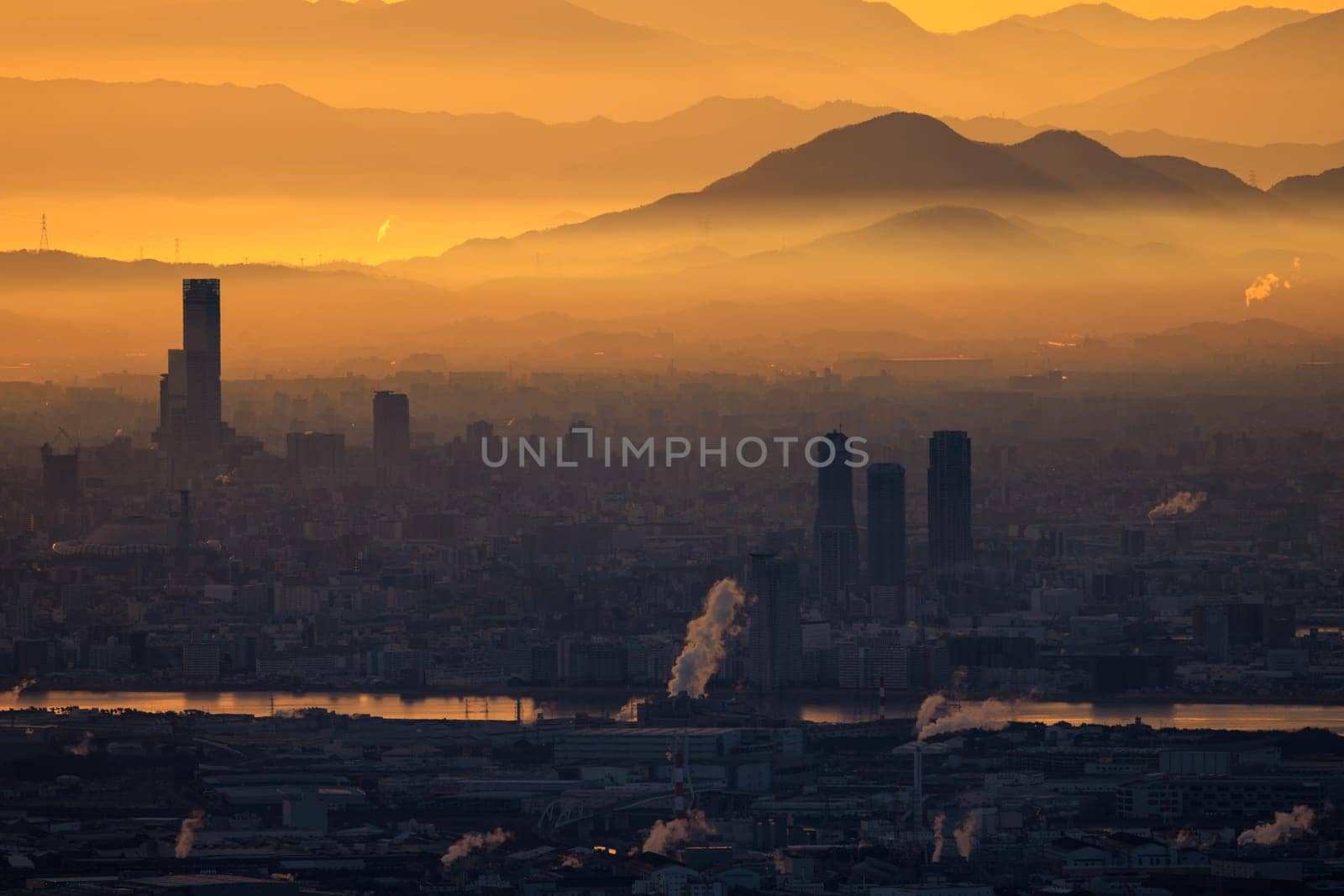 Orange haze from industrial emissions in city by river and mountains at sunrise by Osaze