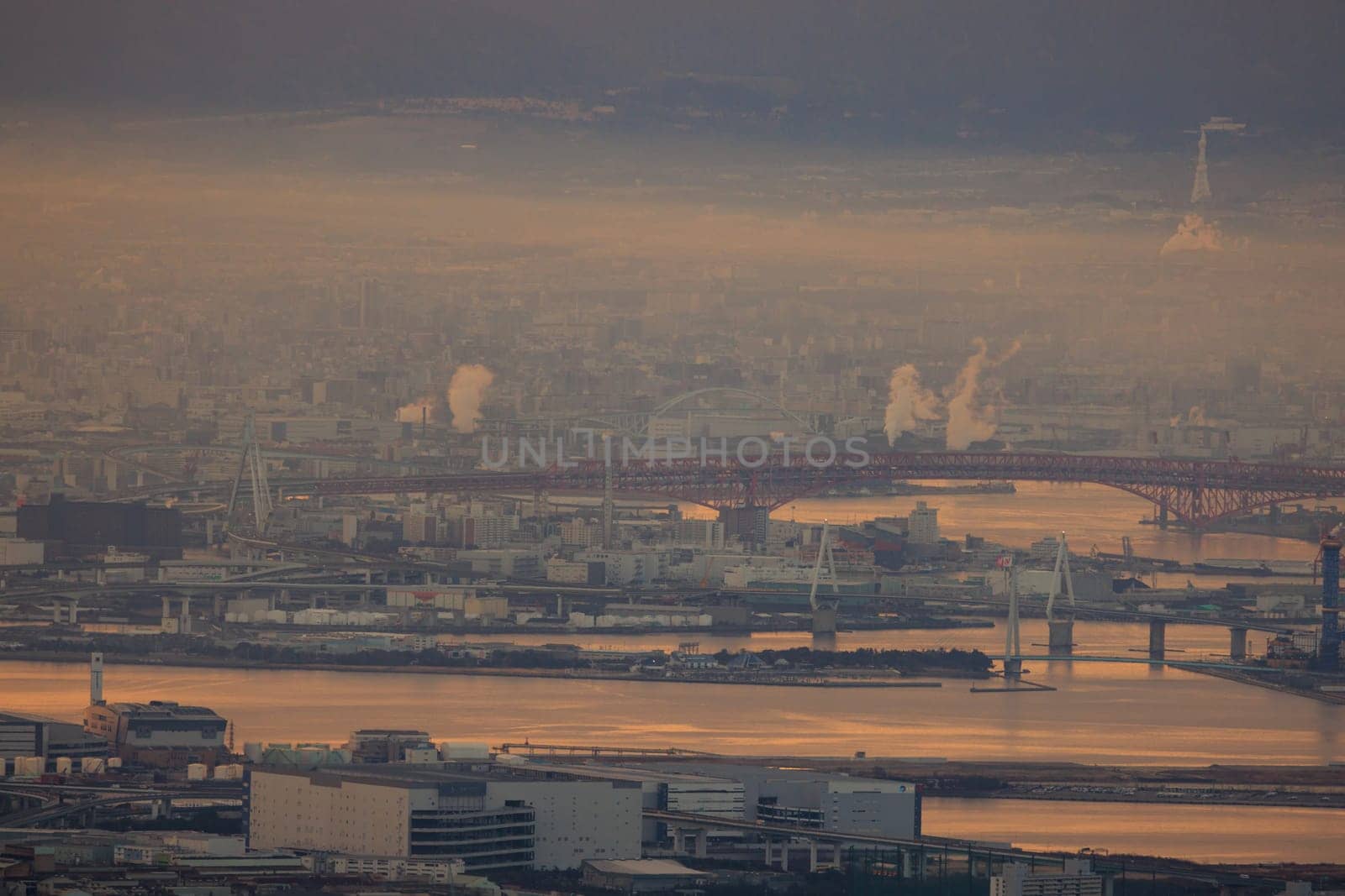 Smoke mixes with atmospheric haze along industrial riverside at dawn. High quality photo
