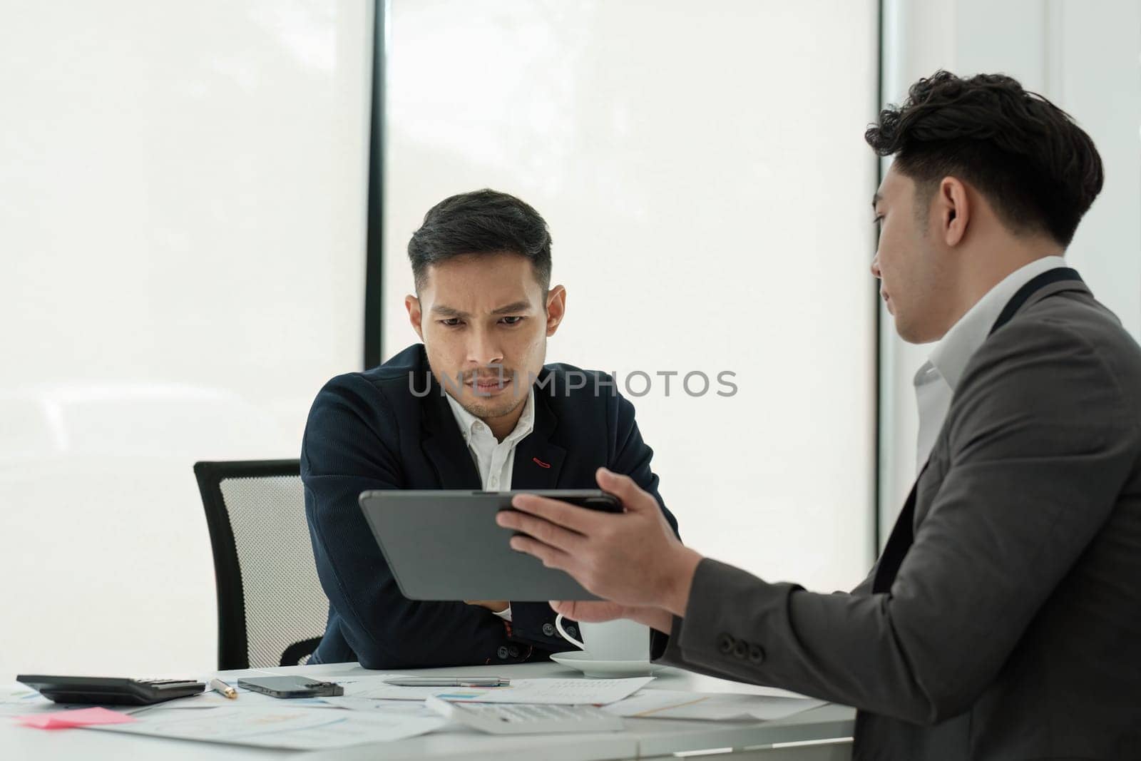 Two serious businessmen discussing project sitting at office desk, using pc laptop, looking at screen, make presentation, create business plan, fulfill task, consider investment..