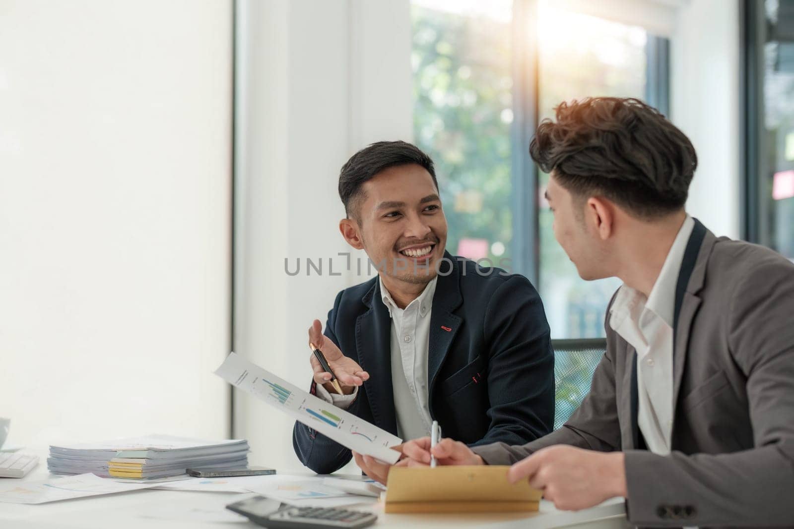 Two business people talk project strategy at office meeting room. Businessman discuss project planning with colleague at modern workplace while having conversation and advice on financial data report