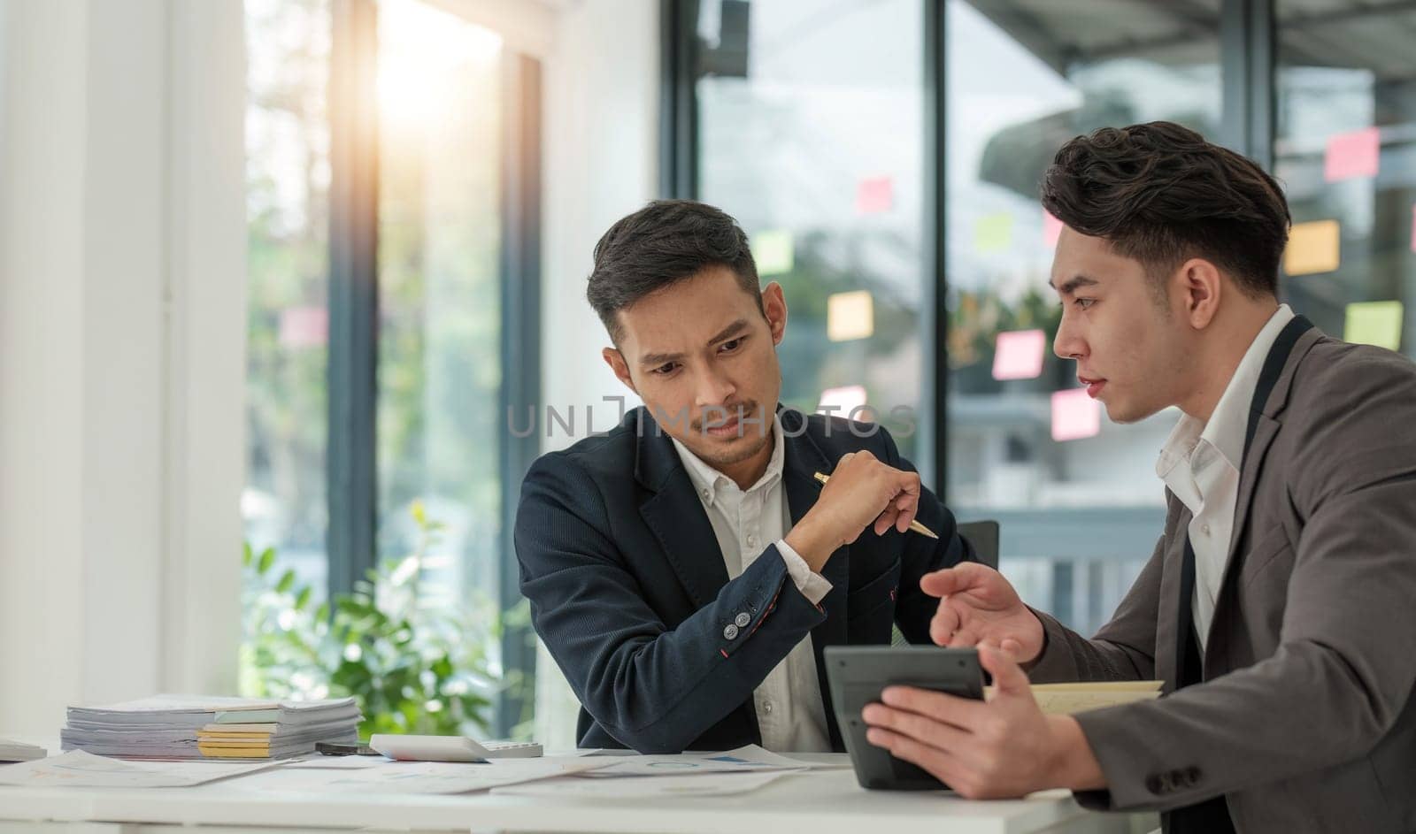 Two business people talk project strategy at office meeting room. Businessman discuss project planning with colleague at modern workplace while having conversation and advice on financial data report