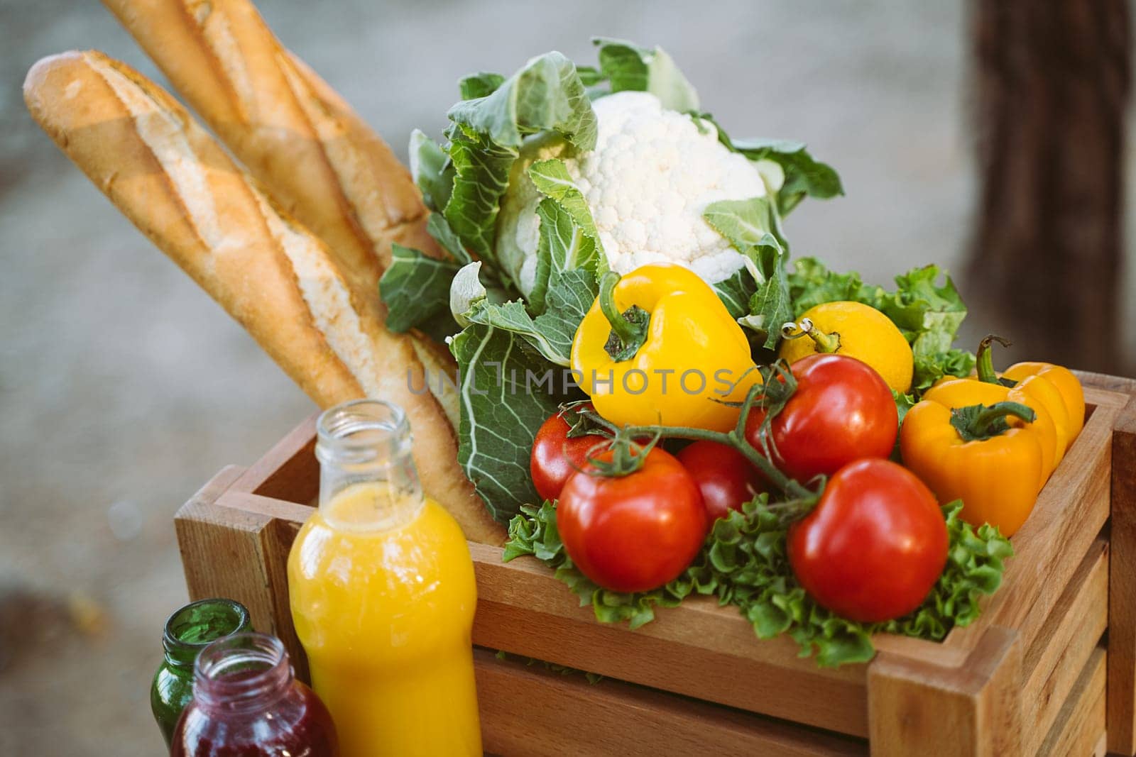 Wooden crate organic farmland vegetables, bread baguettes, fruits, multicolor juice bottles, croissants, dark wood table. Framed crate with cauliflower, sweet pepper, tomatoes, yellow quince, apples