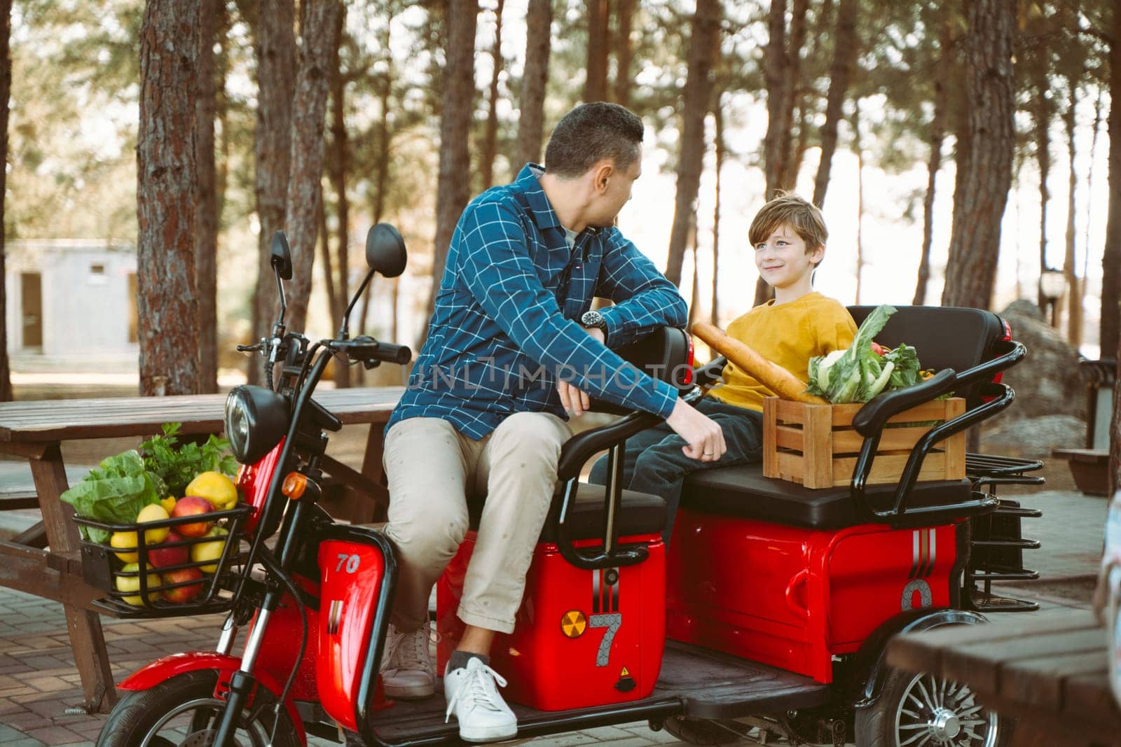 Farmer father and school boy kid delivered wooden crates with vegetables to camp site for picnic. Dad man male and son tourists delivered groceries on electric tricycle vehicle in the forrest