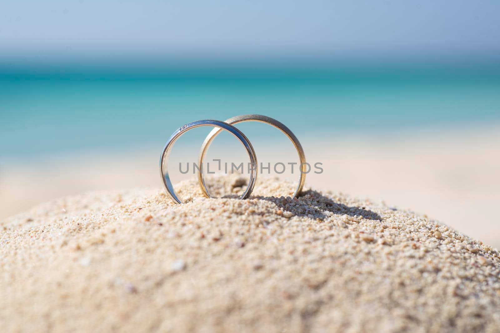 Pair wedding rings in sand on tropical beach by paulvinten