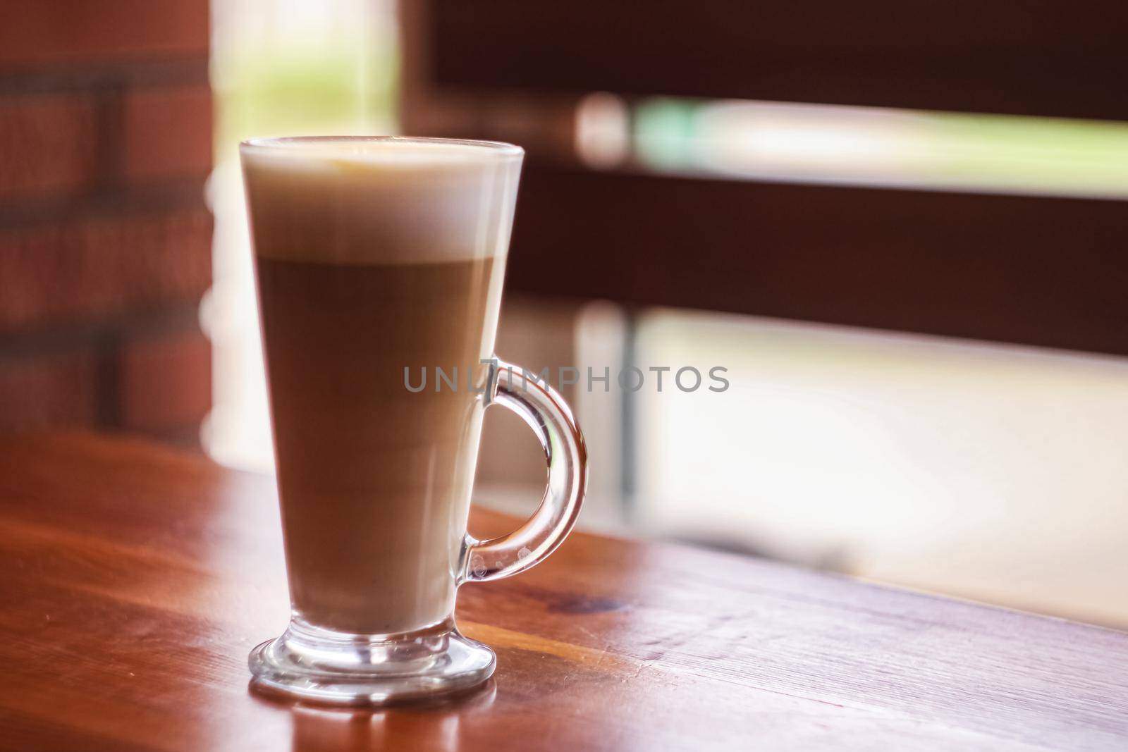Large glass cup of coffee on a wooden table by the window, copy space