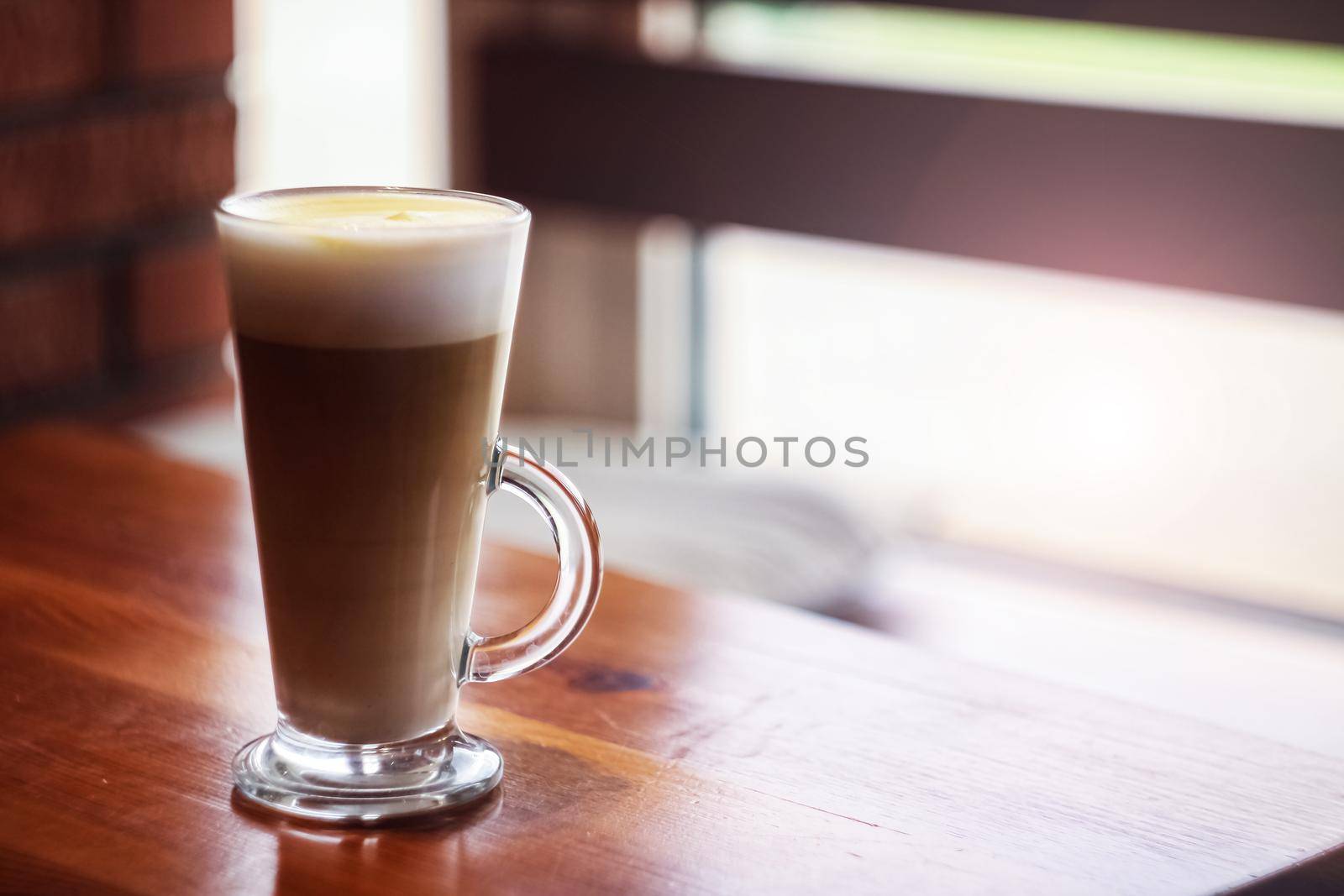 Large glass cup of coffee on a wooden table by the window, copy space