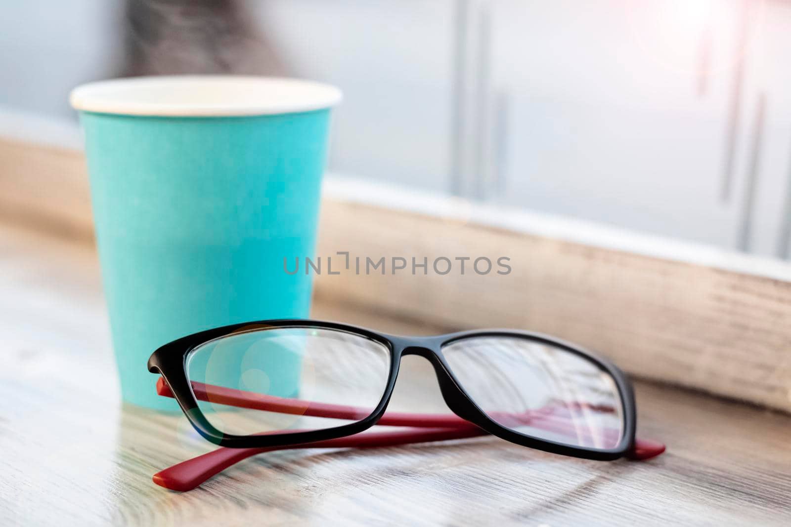 Blue paper cup with coffee and glasses on a wooden table