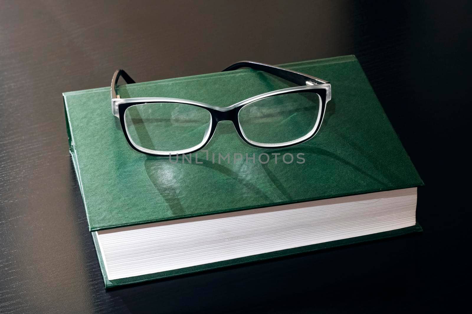 Black glasses on a book on a wooden table close up