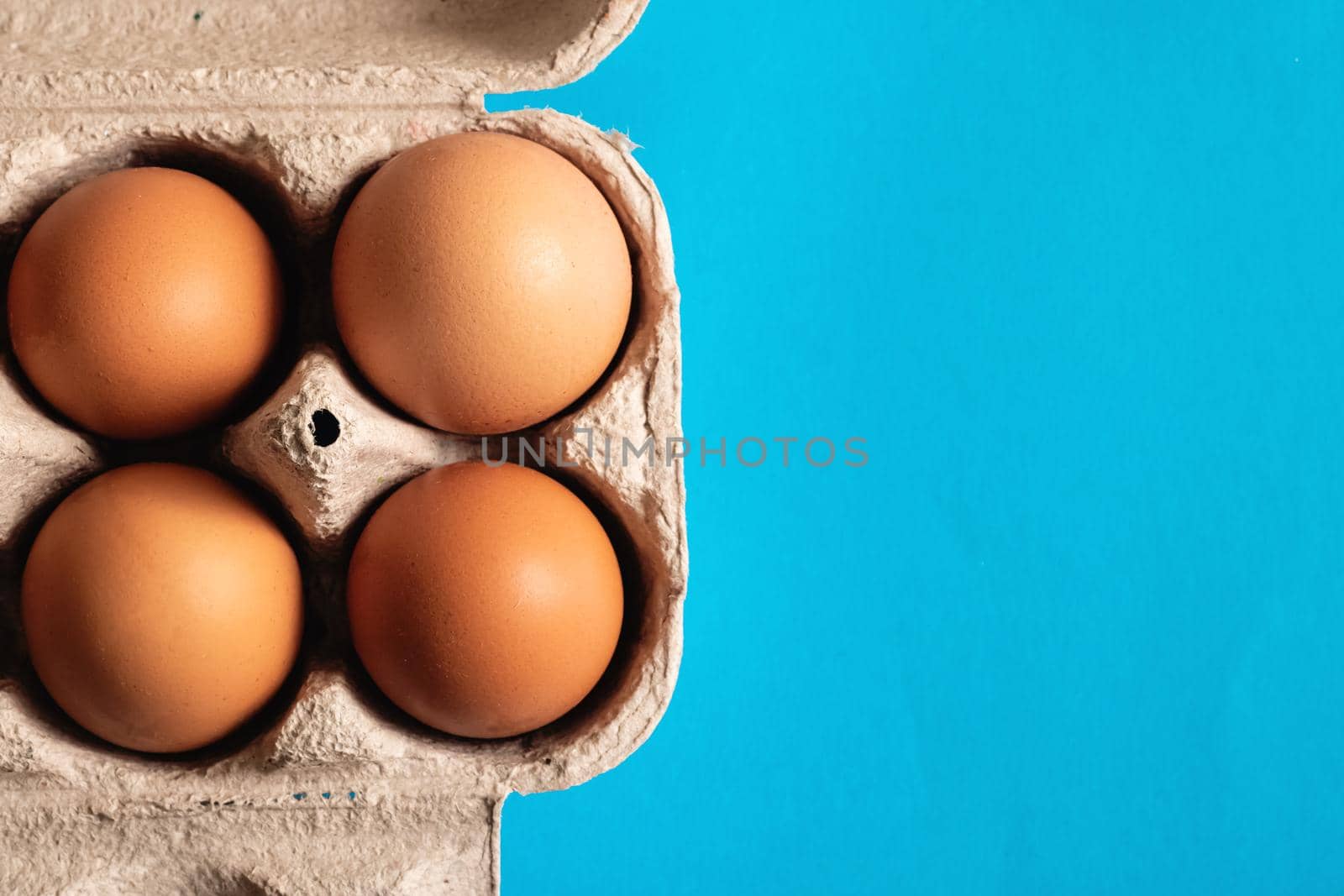 Chicken eggs in a white cardboard box close up on blue background, copy space