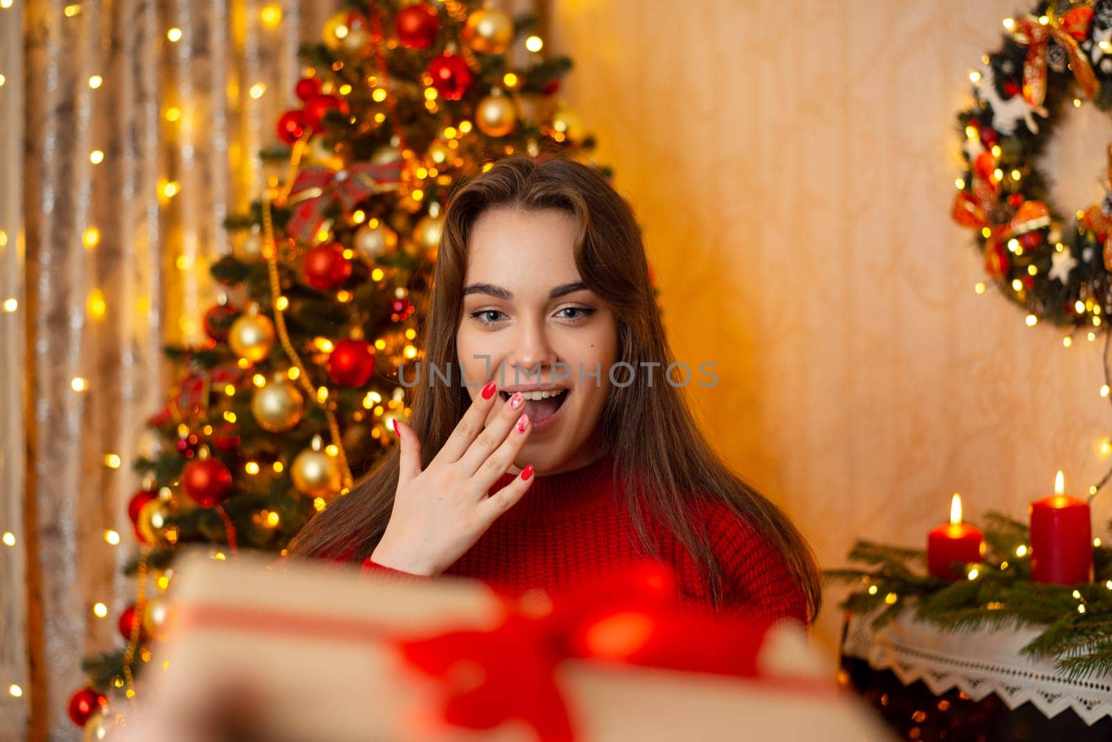 Happy surprised girl receiving present for Christmas, standing in festive room with decorated Christmas tree