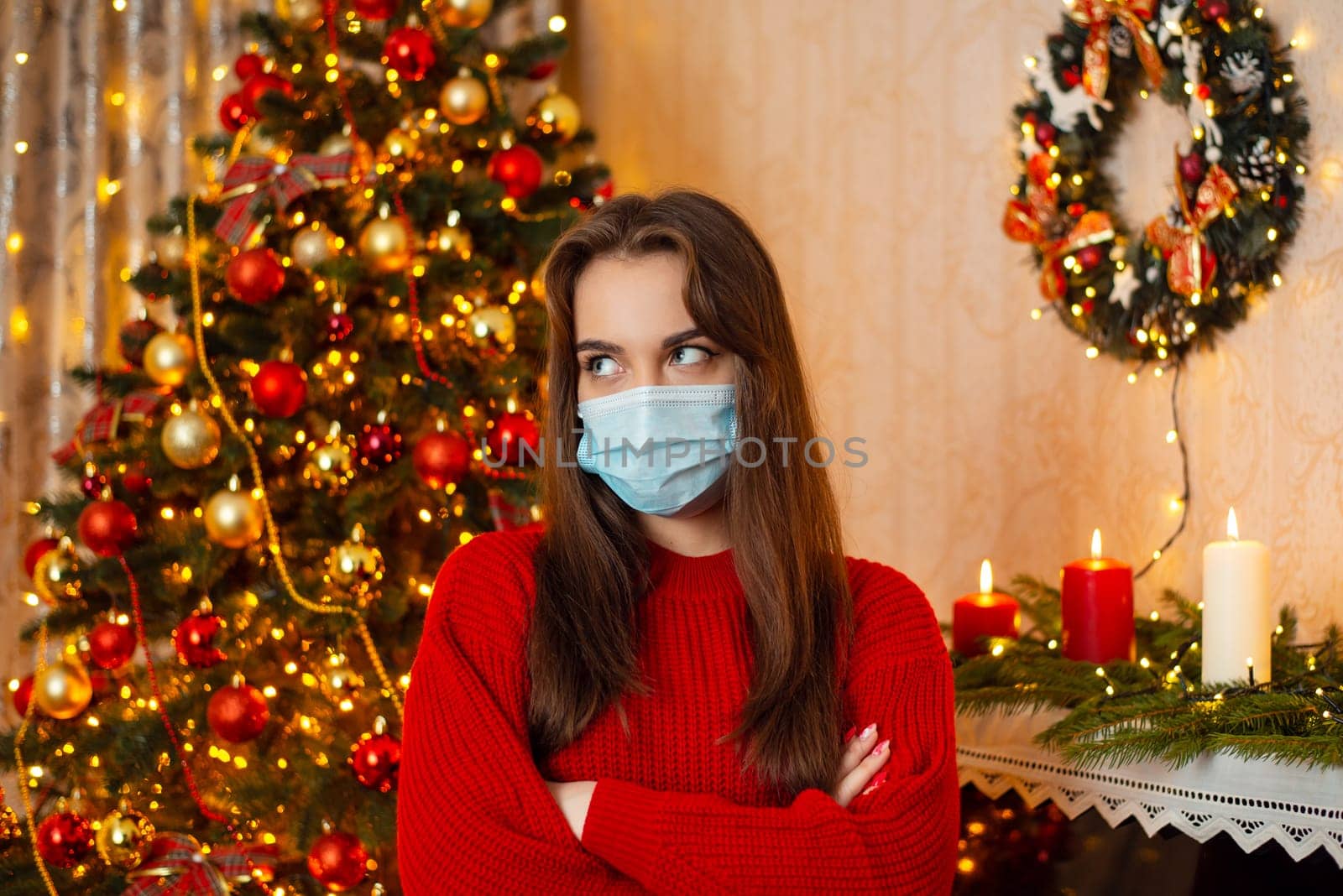 Portrait of a girl, sick and tired of wearing protective medical masks in decorated room with Christmas tree in the background