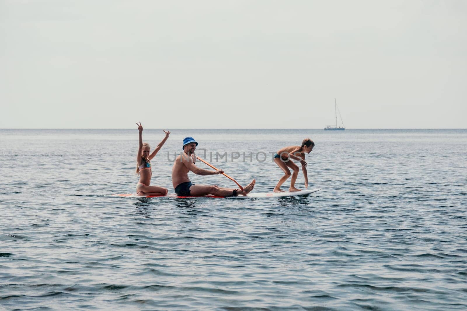 Father and his adorable little son and daughter sitting on stand up board having fun during summer beach vacation