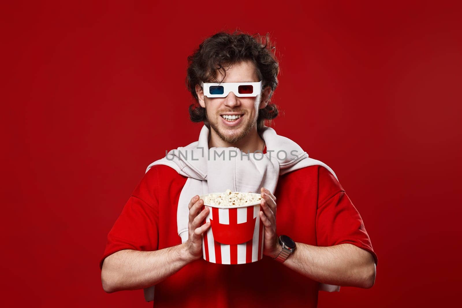 happy smiling bearded man in 3d-glasses holding big bucket of popcorns on red background