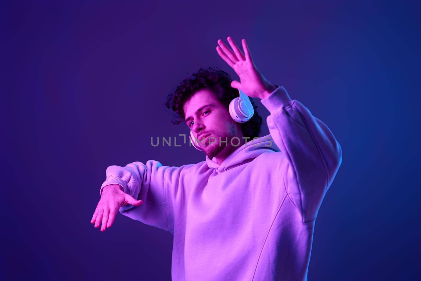 handsome bearded man with headphones in sweatshirt enjoying favorite music on blue background. Neon lighting