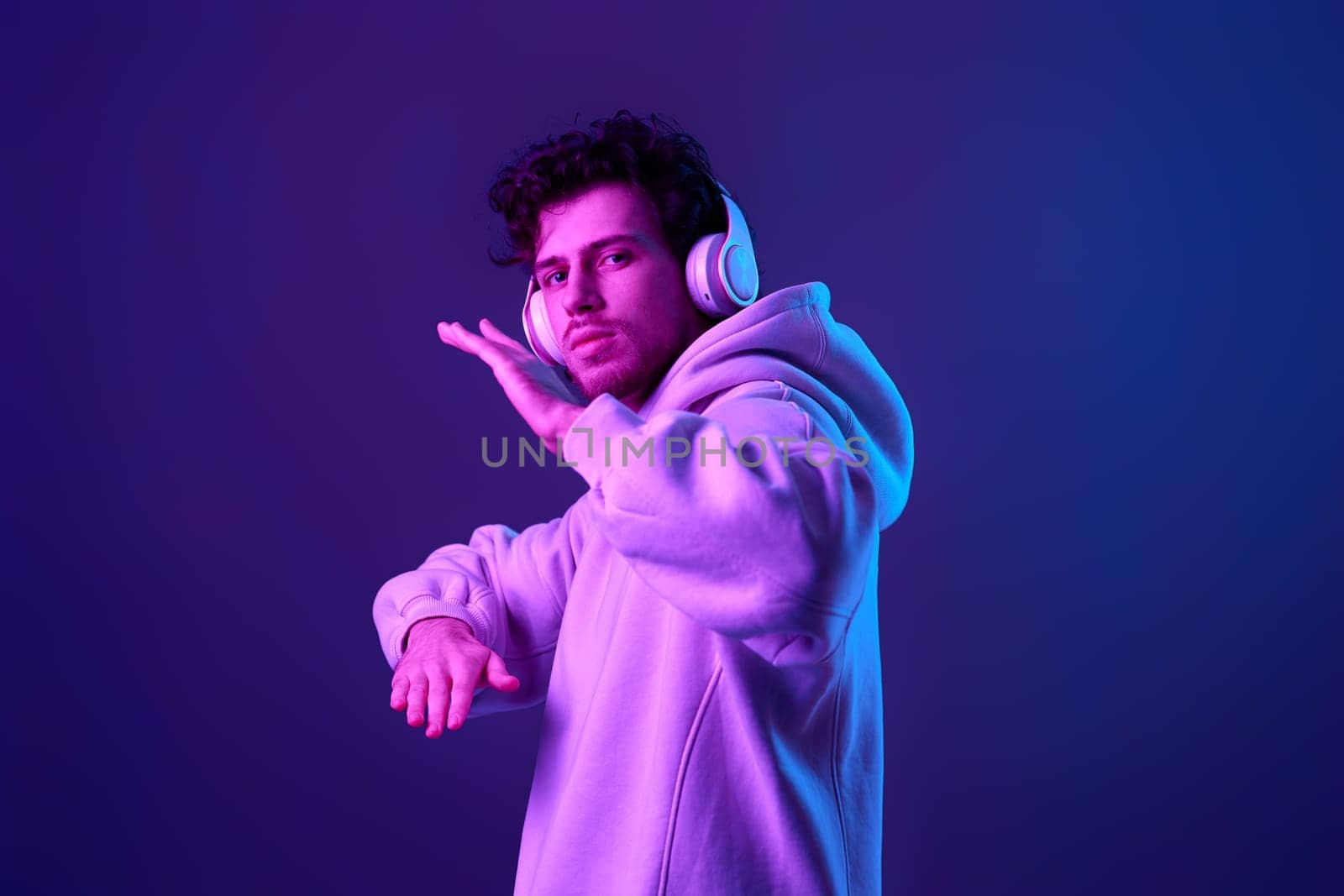 handsome man with headphones in sweatshirt enjoying favorite tracks on blue background. Neon lighting