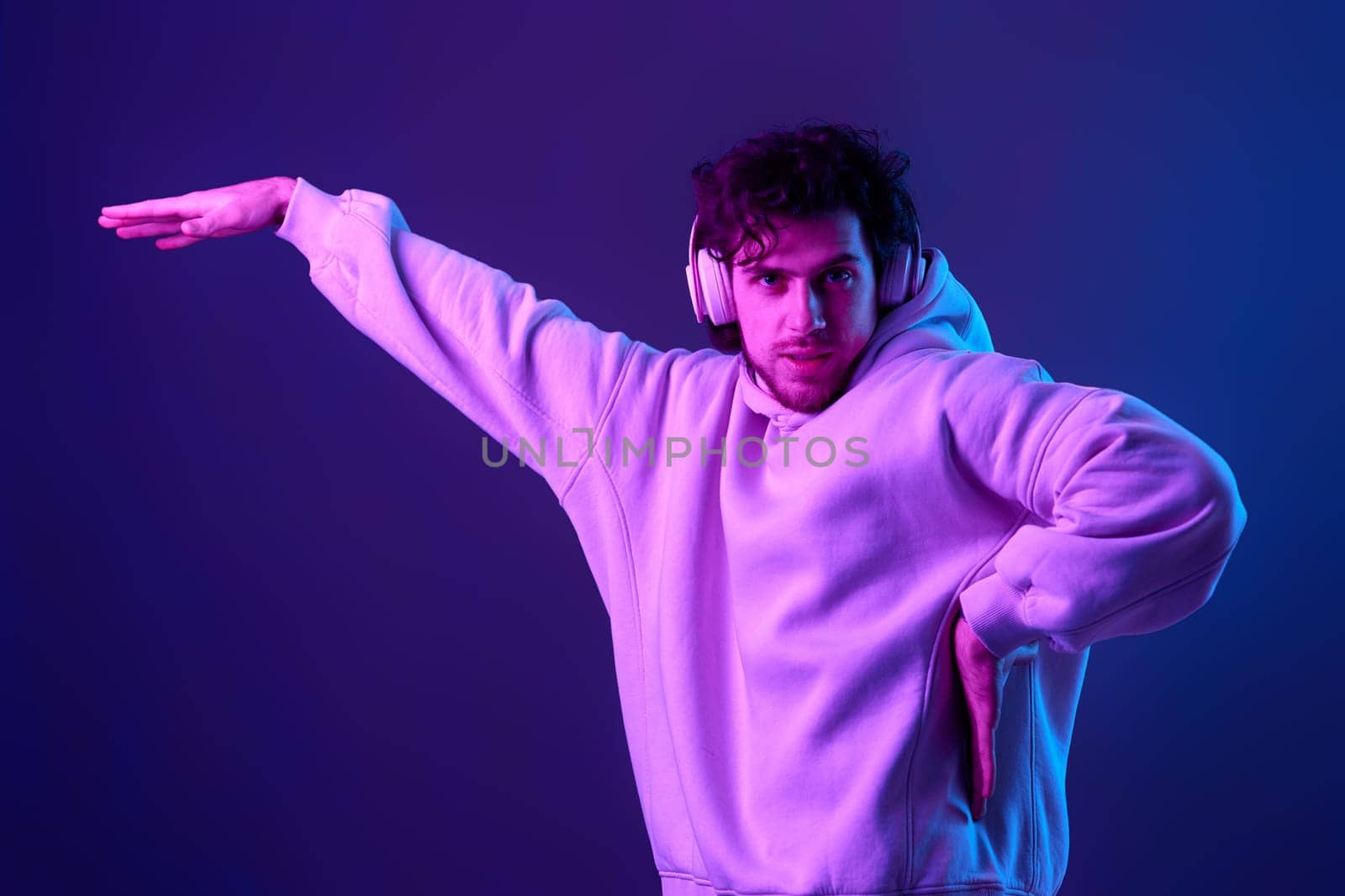 handsome bearded man with headphones in sweatshirt enjoying favorite tracks on blue background. Neon lighting