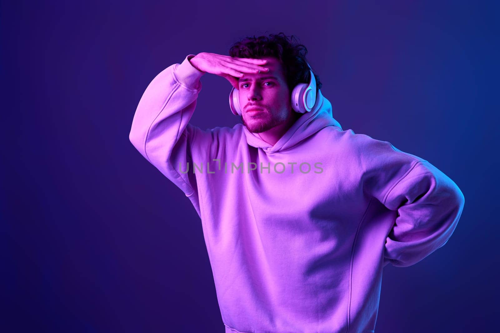 handsome man with headphones in sweatshirt enjoying favorite tracks on blue background. Neon lighting