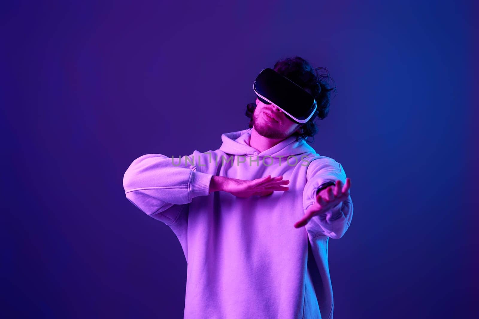 man in sweatshirt using virtual reality headset on blue background. Neon lighting