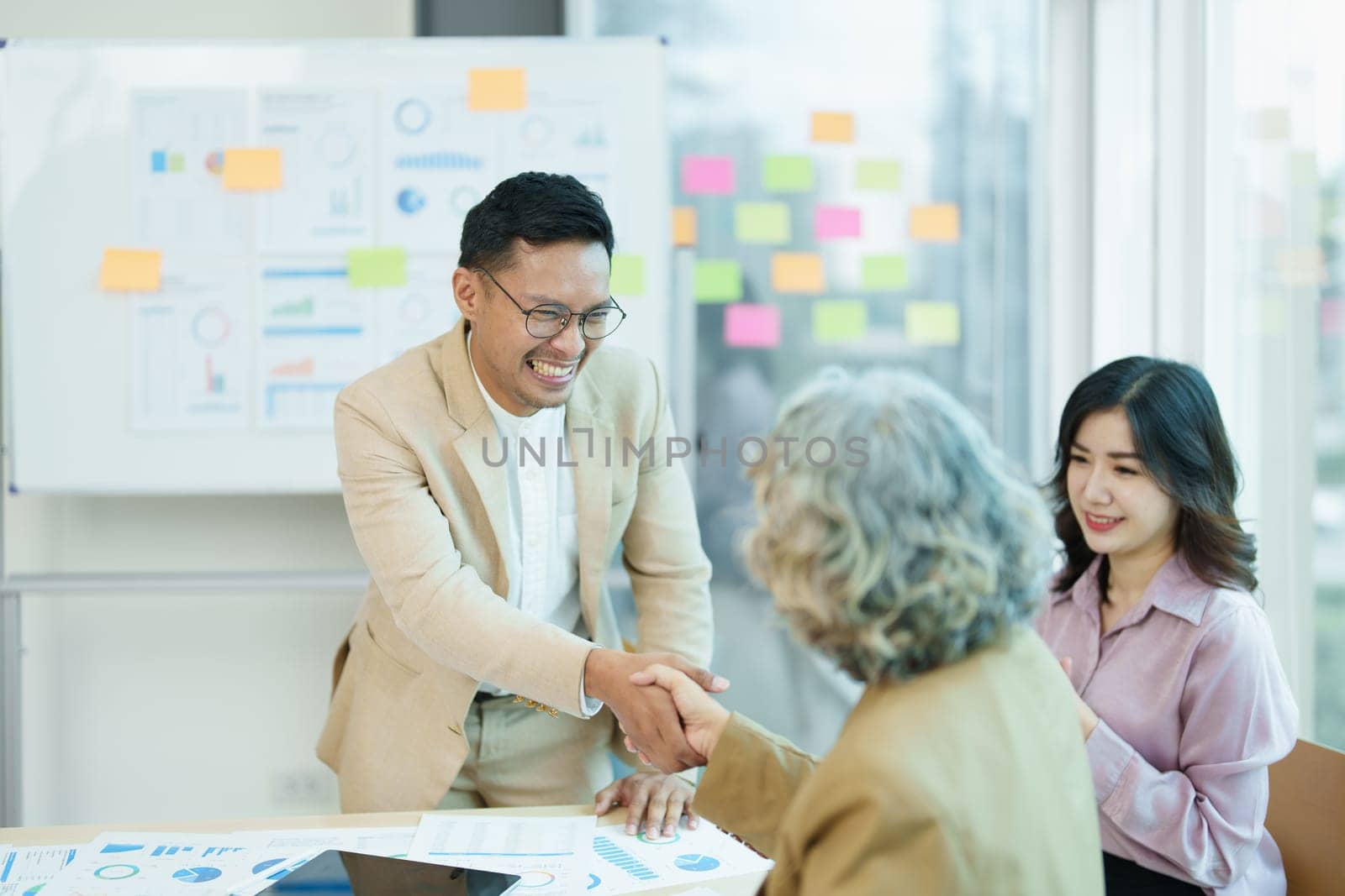 Asian entrepreneurs handshakes to congratulate the agreement between the two companies to enhance investment and financial strength. deal concept by Manastrong