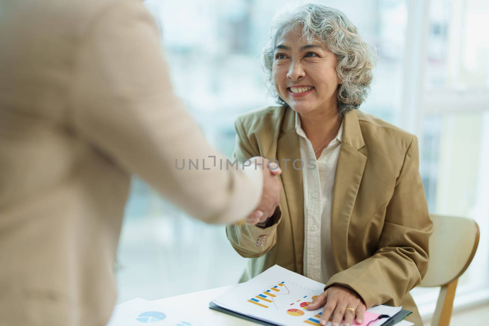 Asian entrepreneurs handshakes to congratulate the agreement between the two companies to enhance investment and financial strength. deal concept by Manastrong