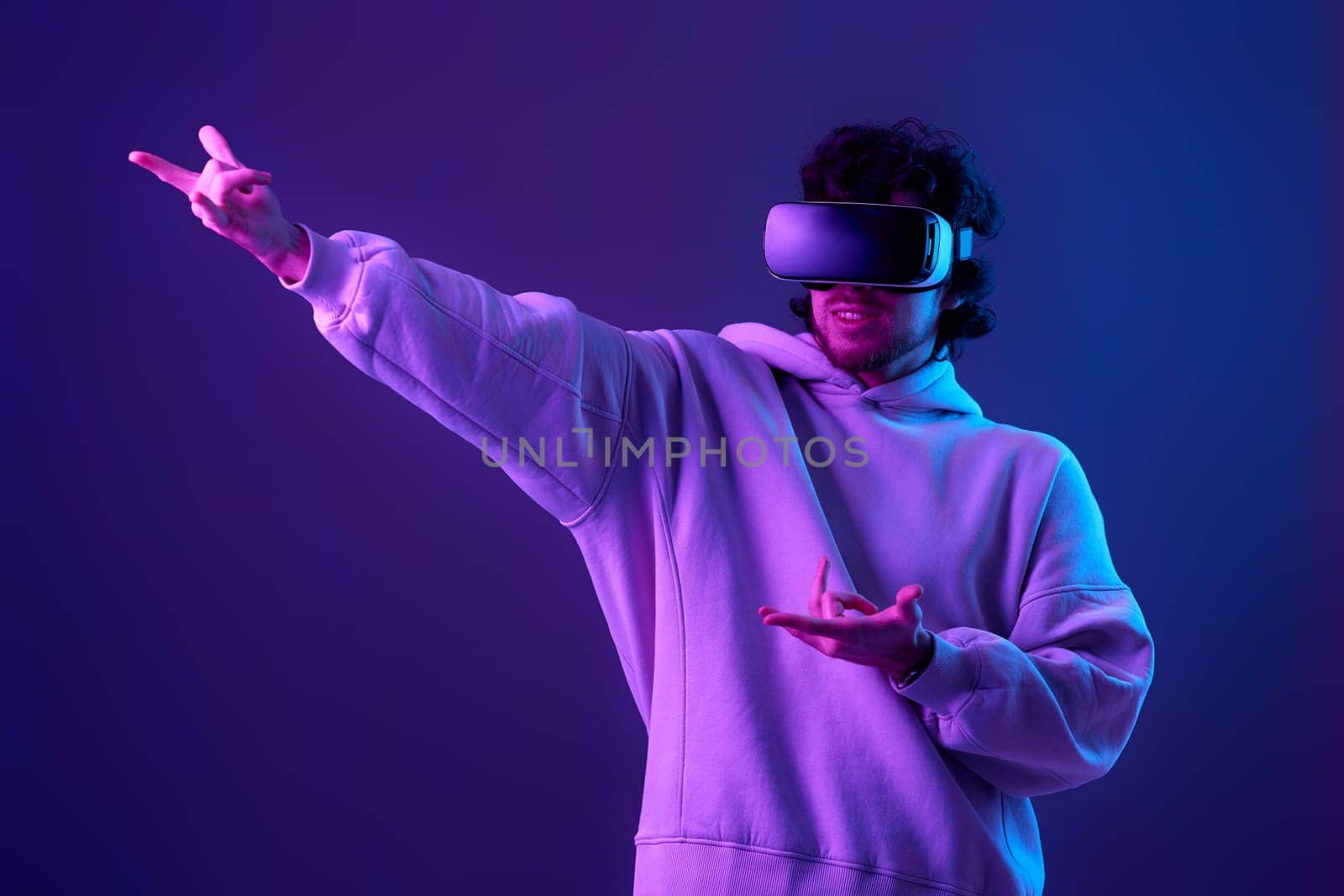 man in sweatshirt using virtual reality headset on blue background. Neon lighting