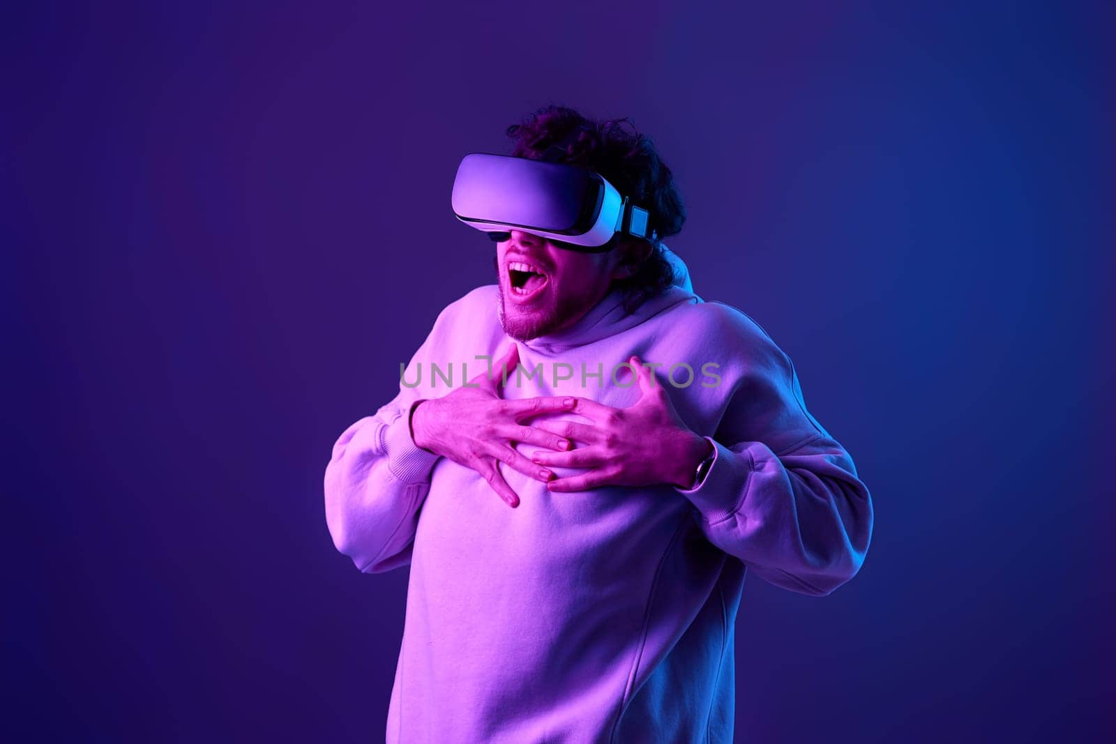 man in sweatshirt using virtual reality glasses on blue background. Neon lighting