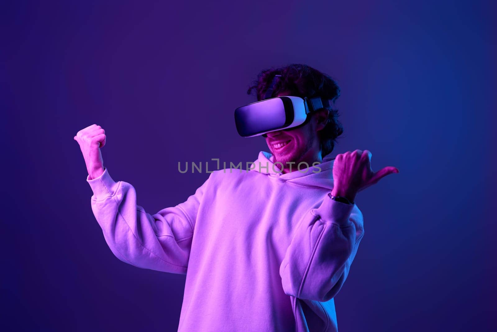 man in sweatshirt using virtual reality headset on blue background. Neon lighting