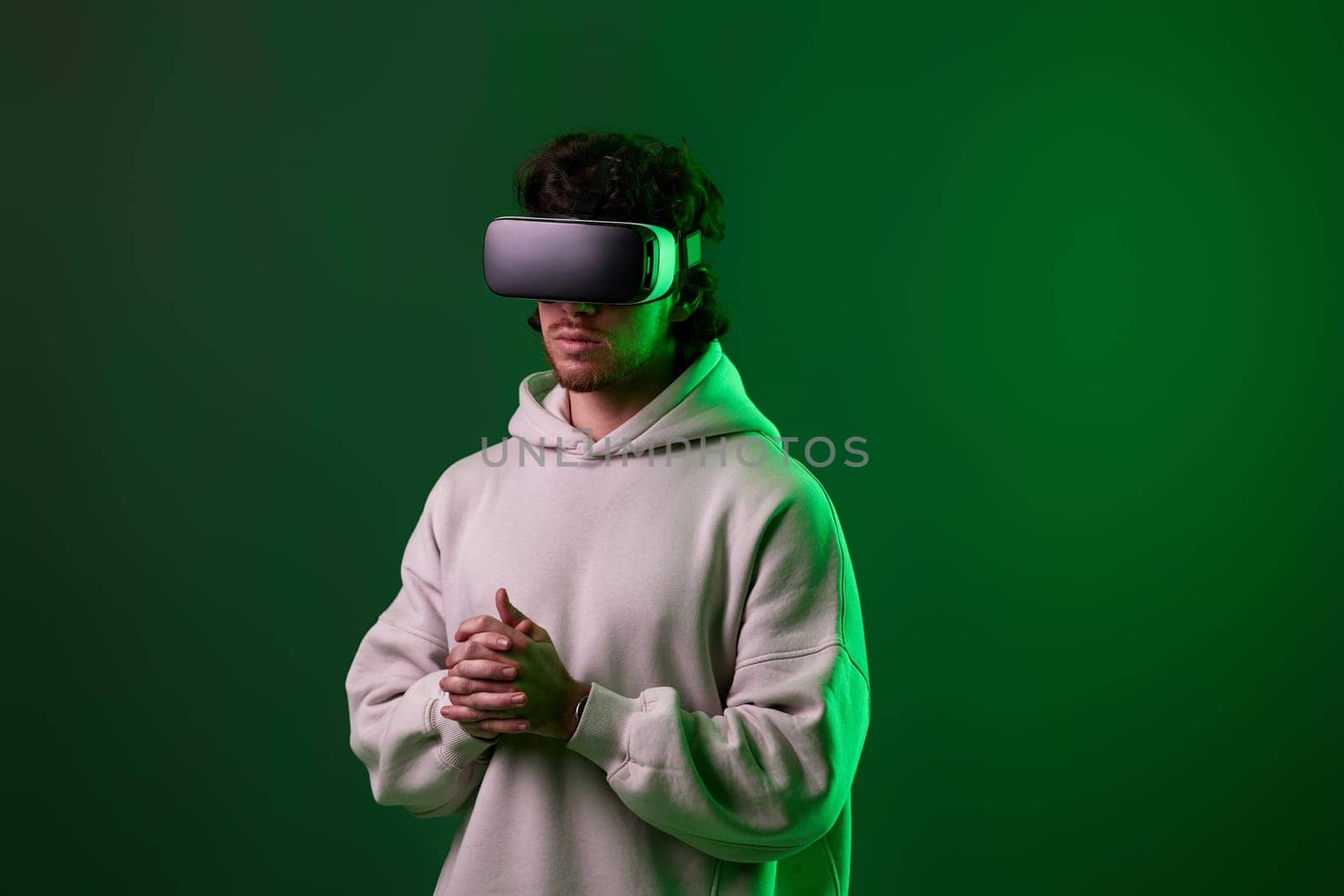 man in sweatshirt using virtual reality headset on green background. Neon lighting