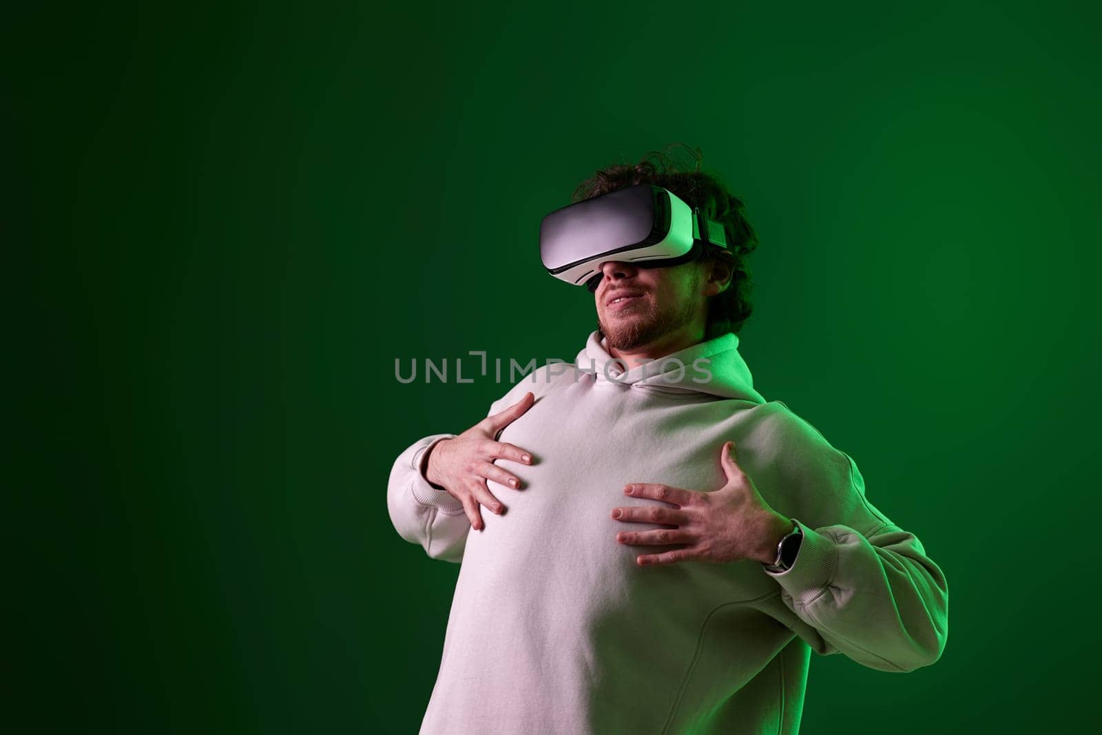 man in sweatshirt using virtual reality headset on green background. Neon lighting