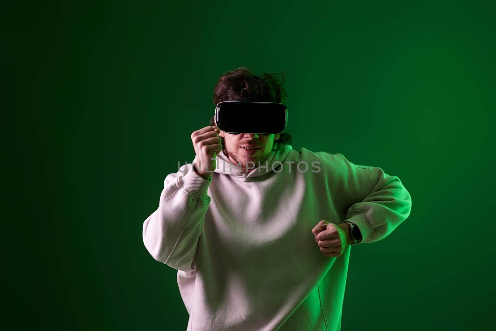 man in sweatshirt using virtual reality headset and playing video games on green background. Neon lighting