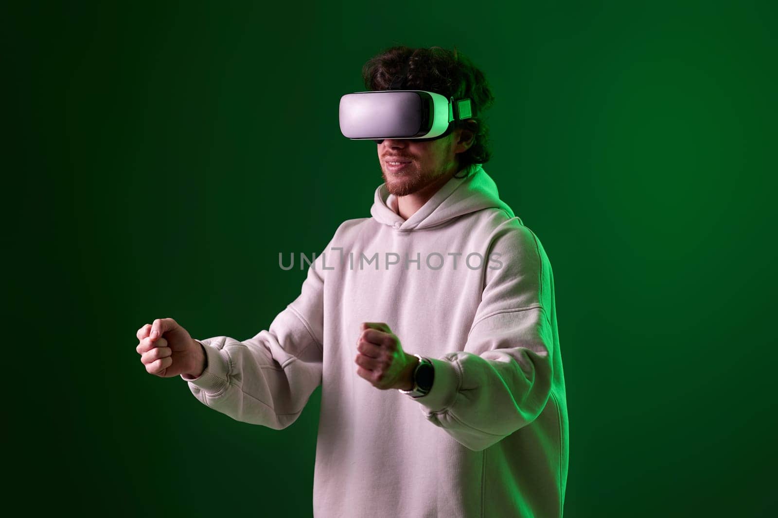 man in sweatshirt using virtual reality headset and playing video games on green background. Neon lighting