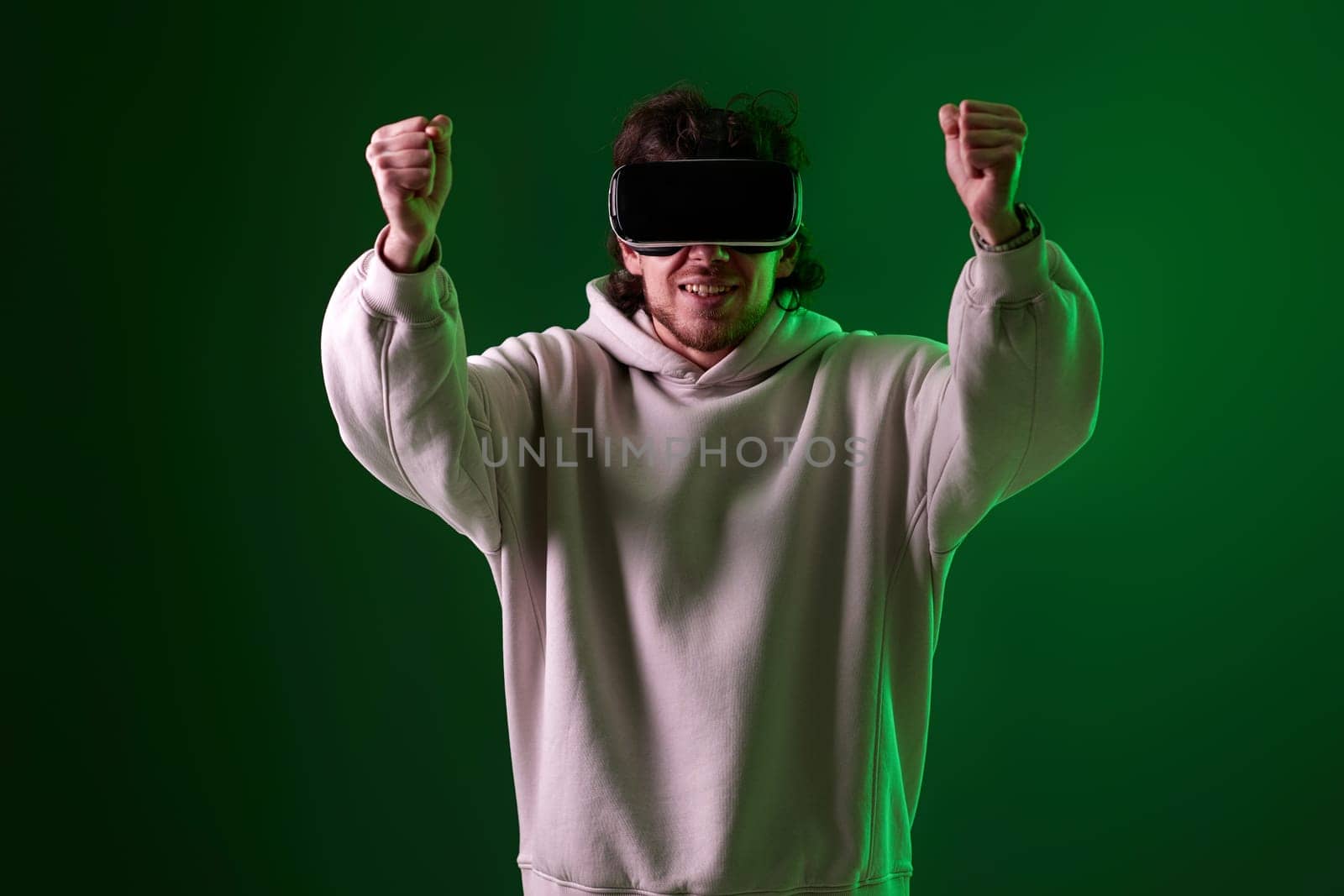 man in sweatshirt using virtual reality headset on green background. Neon lighting