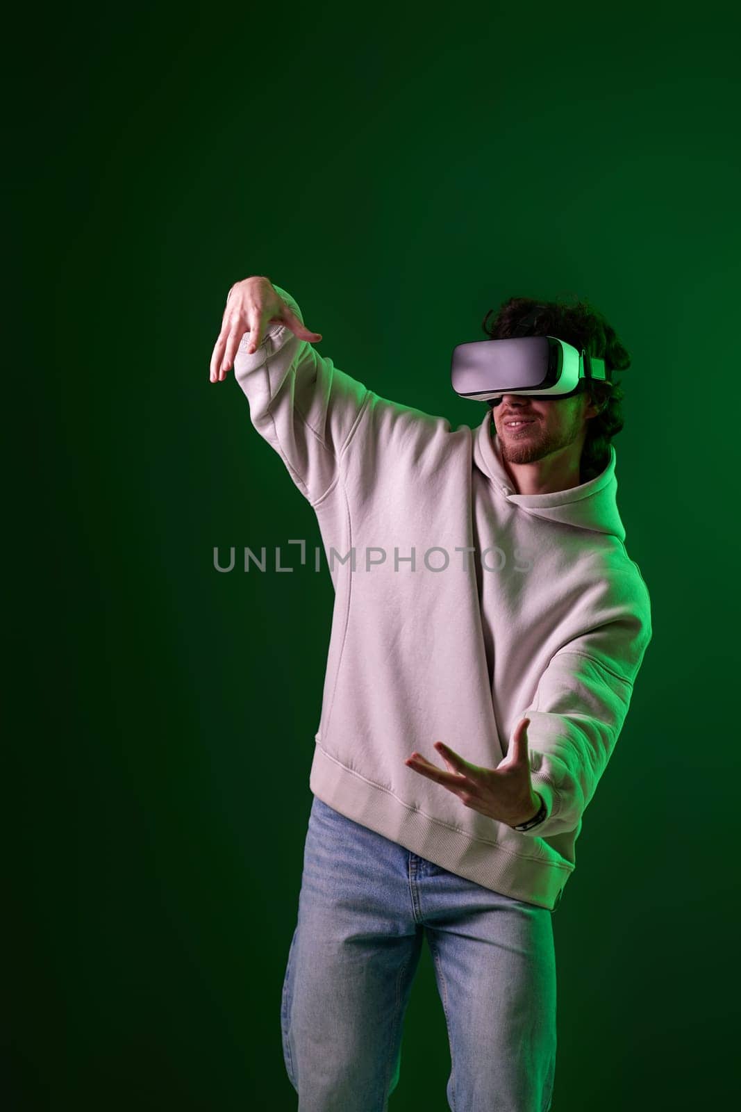 man in vr glasses and sweatshirt playing video games with his friends on green background. Neon lighting