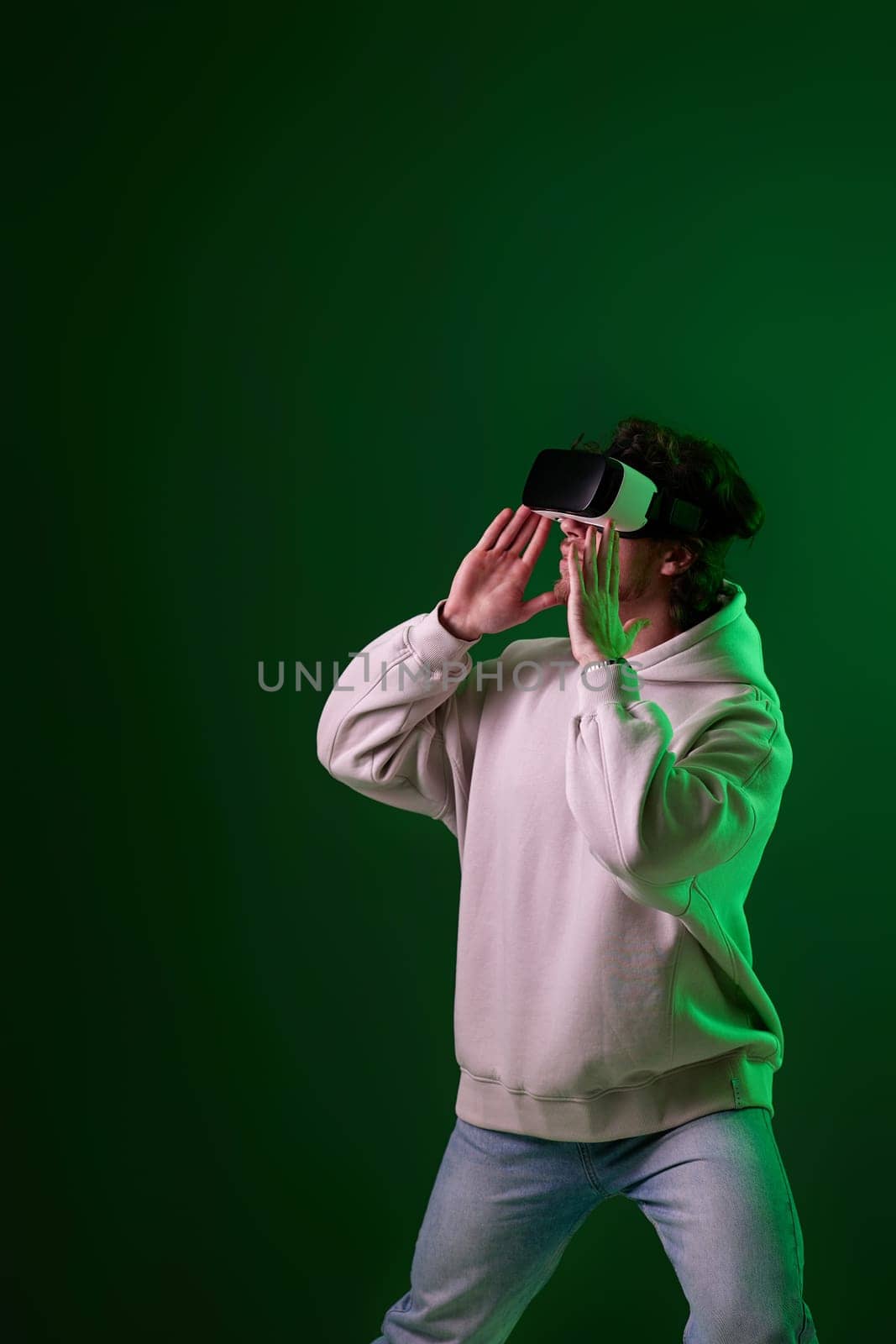 man in sweatshirt using virtual reality headset on green background. Neon lighting