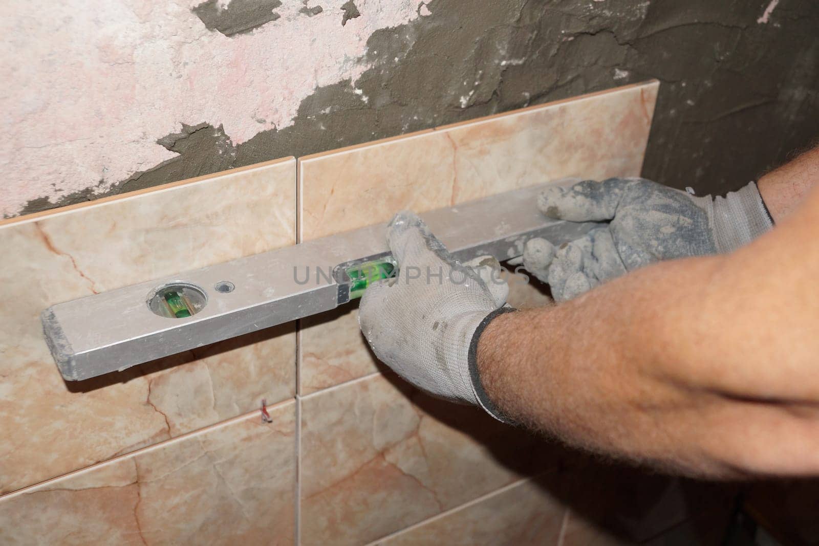 a worker checks the glued ceramic tiles with a building level by Annado