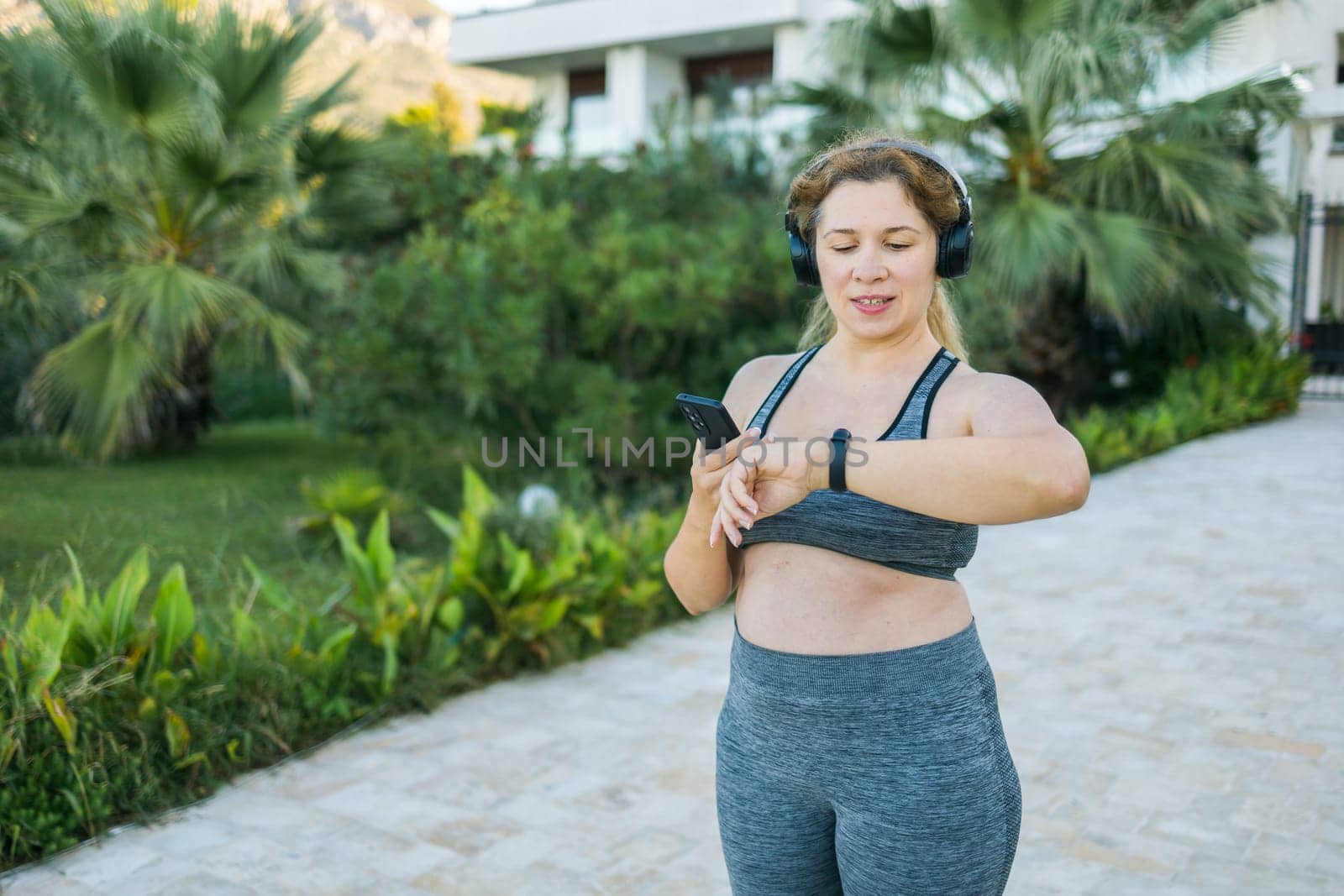 Fat woman checking time or heart rate from smart watch. Exercise or running outdoors for weight loss idea concept. Wellness and wellbeing copy space and empty space for text or advertising by Satura86