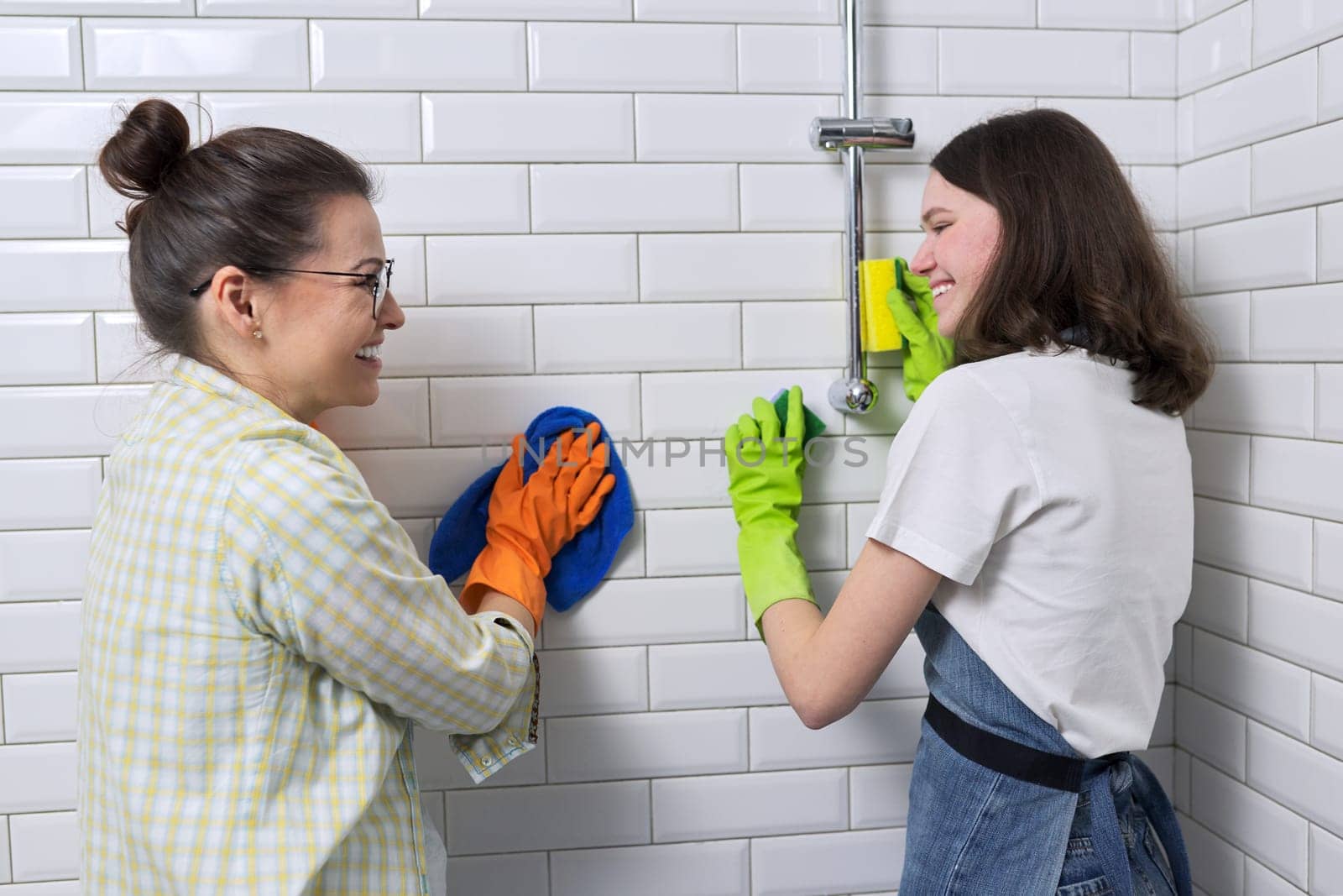 Mother and teenager daughter cleaning together in bathroom. Girl helping mother clean at home. Teens and parents, relationships, cleanliness and housekeeping, household duties
