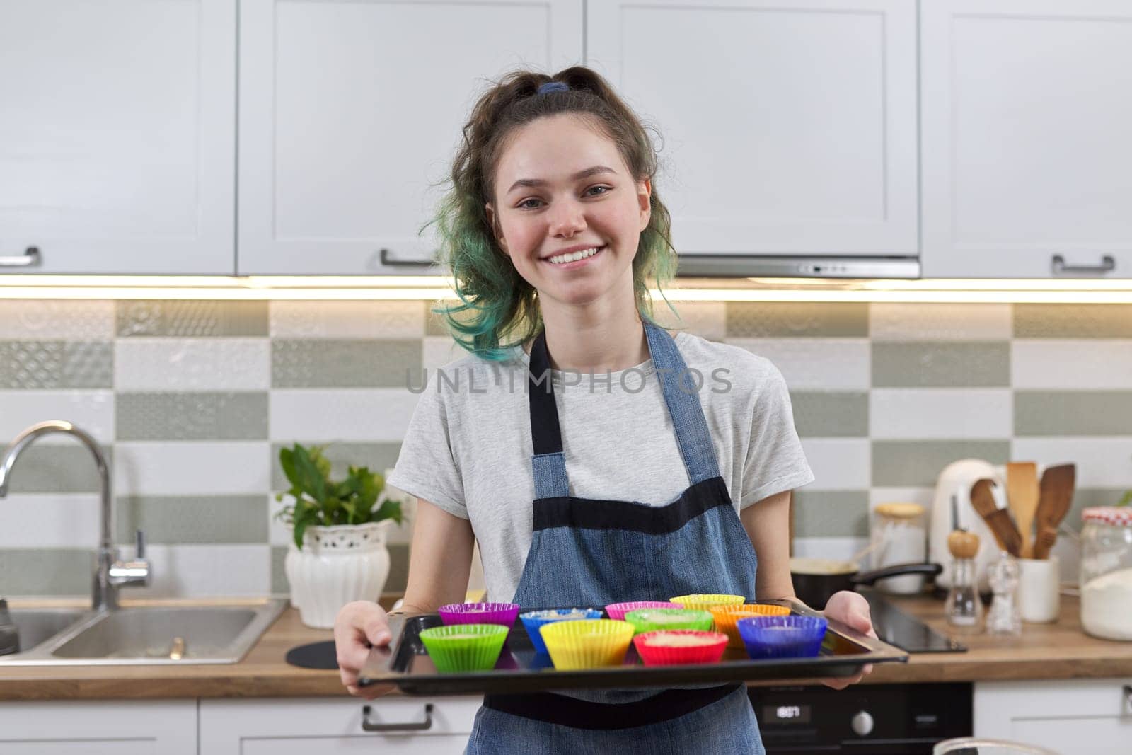 Teen girl in apron in kitchen with tray of preparing raw silicone cupcakes by VH-studio