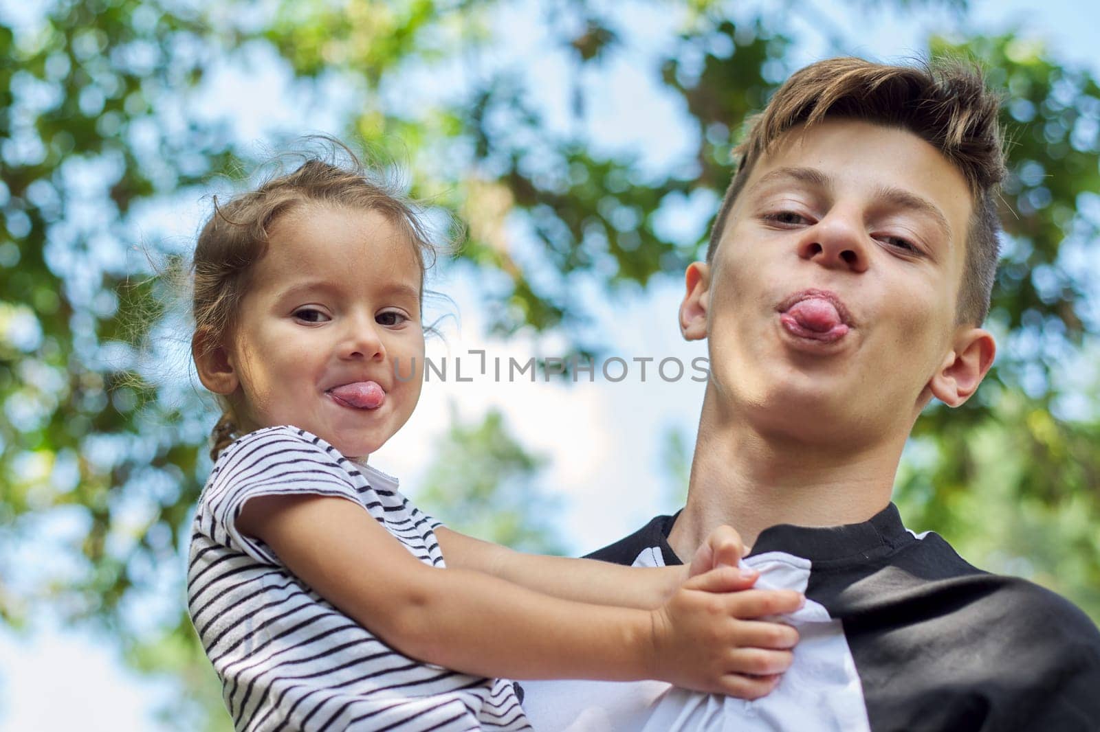Children boy teenager and toddler girl look at the camera and show tongues by VH-studio
